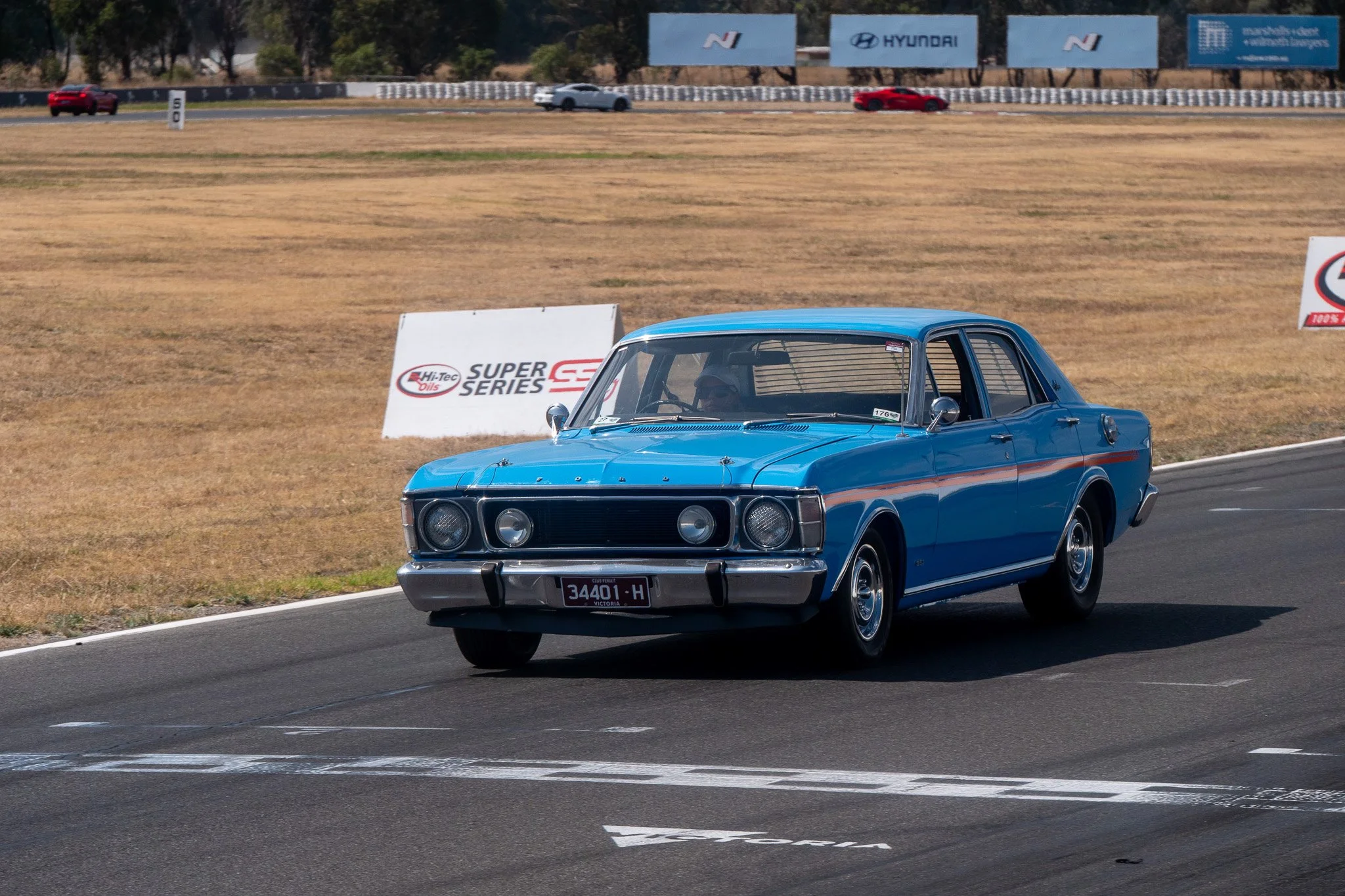 A vintage blue car driving on a race track during a racing event.