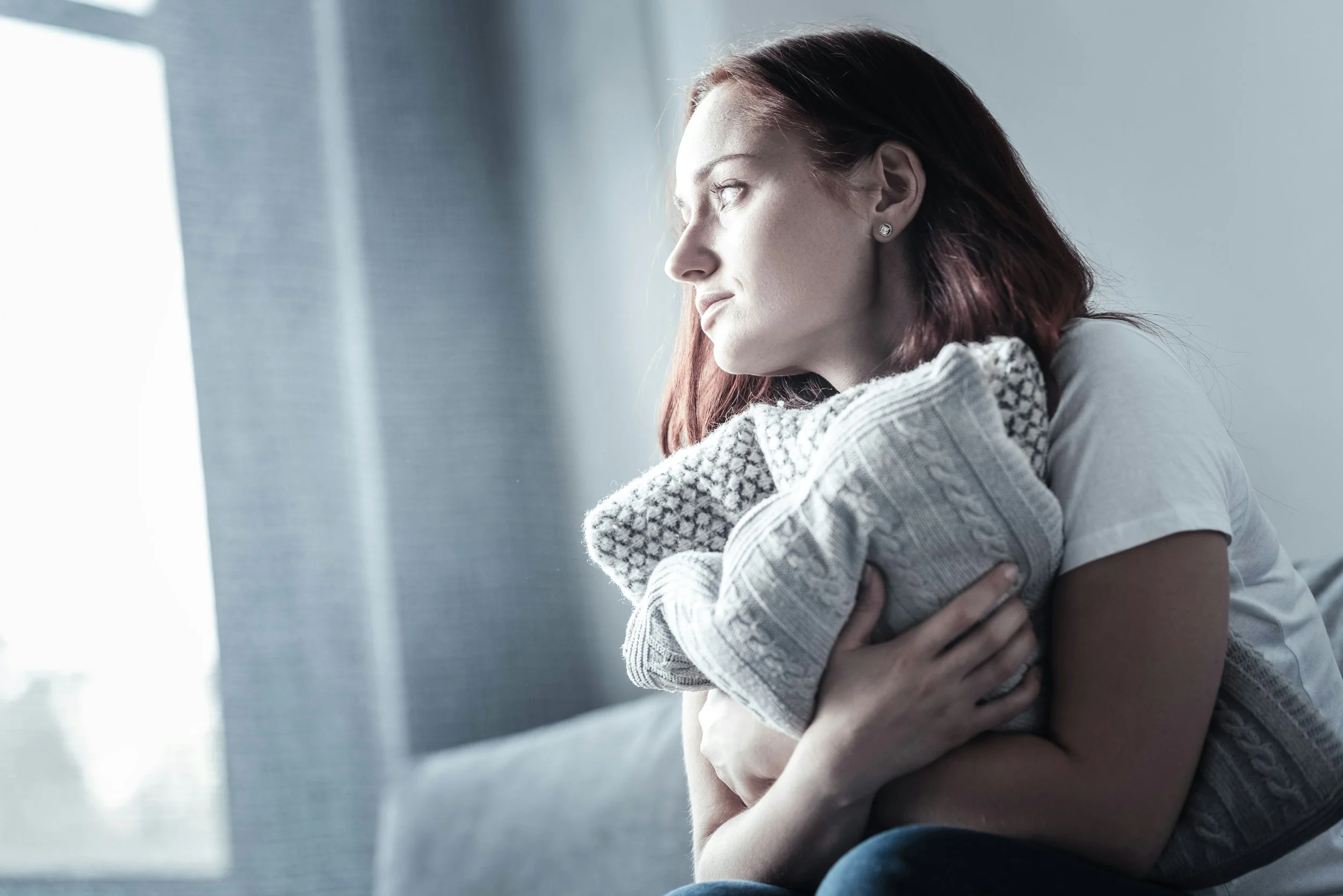 Young woman hugging a pillow while sitting alone, representing coping with social anxiety and emotional overwhelm.