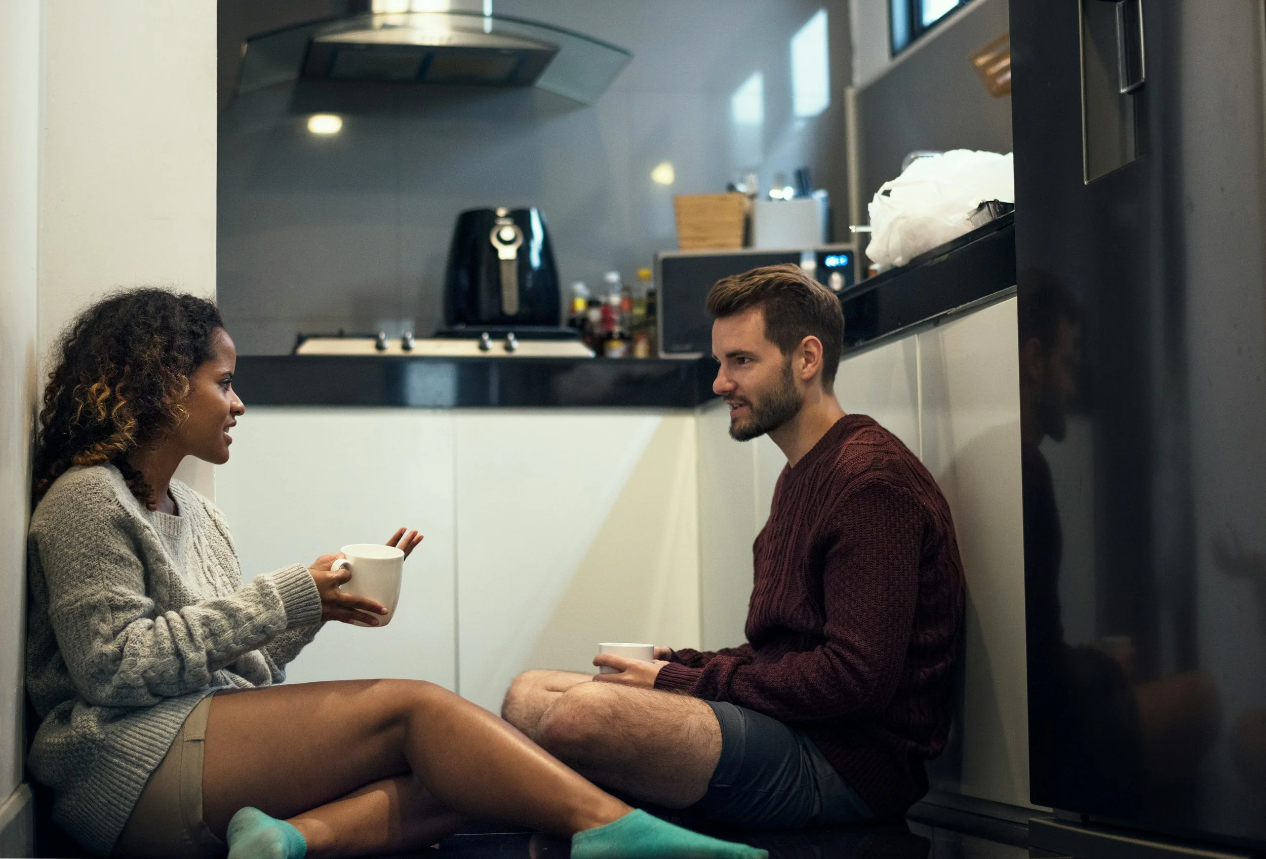 Couple having a serious conversation at a kitchen table, representing communication and recurring conflict in relationships.