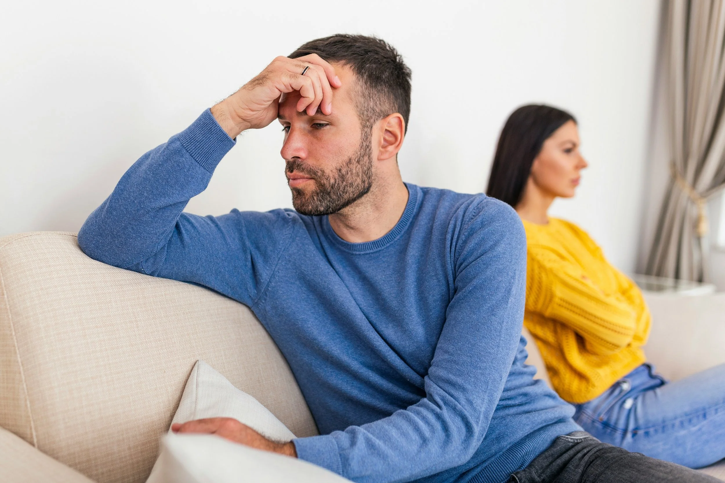 Couple sitting together on a couch while one partner appears distant, representing anxiety about a partner's changing mood in a relationship.