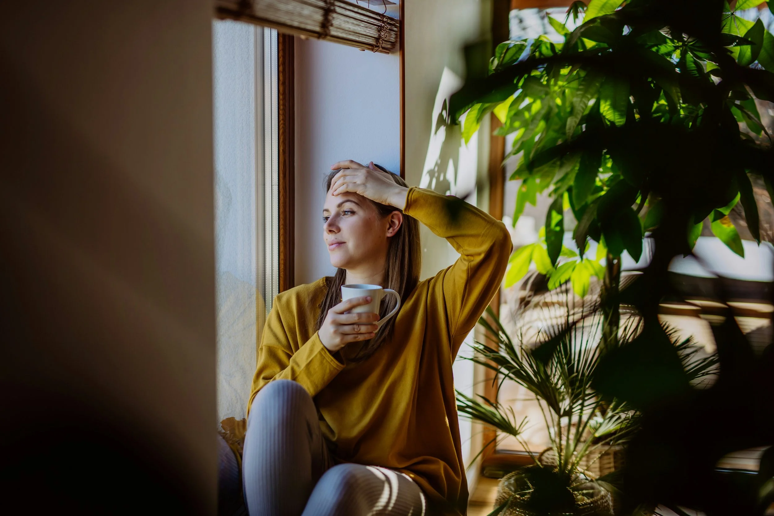 Person sitting peacefully near a sunny window, representing the complicated emotions that can come with experiencing a good day while living with depression.