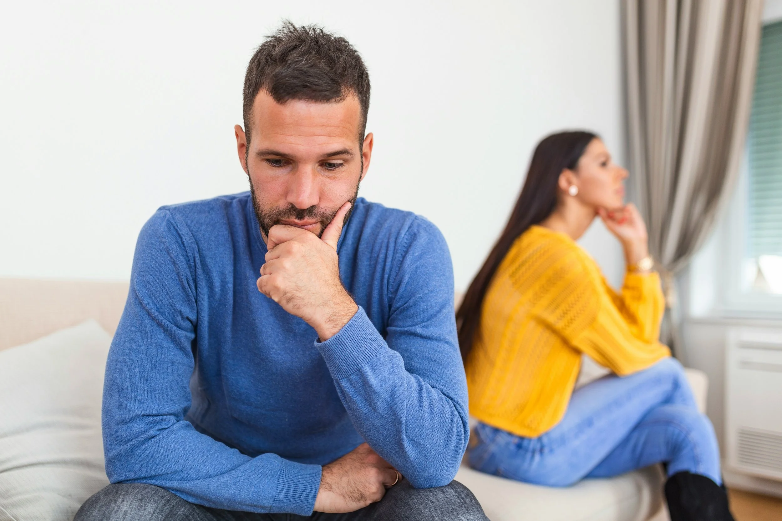 Couple sitting together with visible emotional distance, representing jealousy, insecurity, and attachment-related relationship stress
