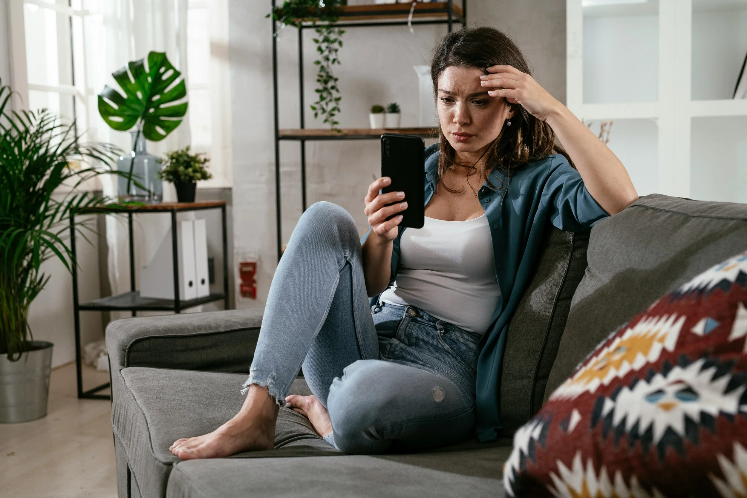 Thoughtful young woman looking at her phone while experiencing emotional stress related to social comparison and self-worth