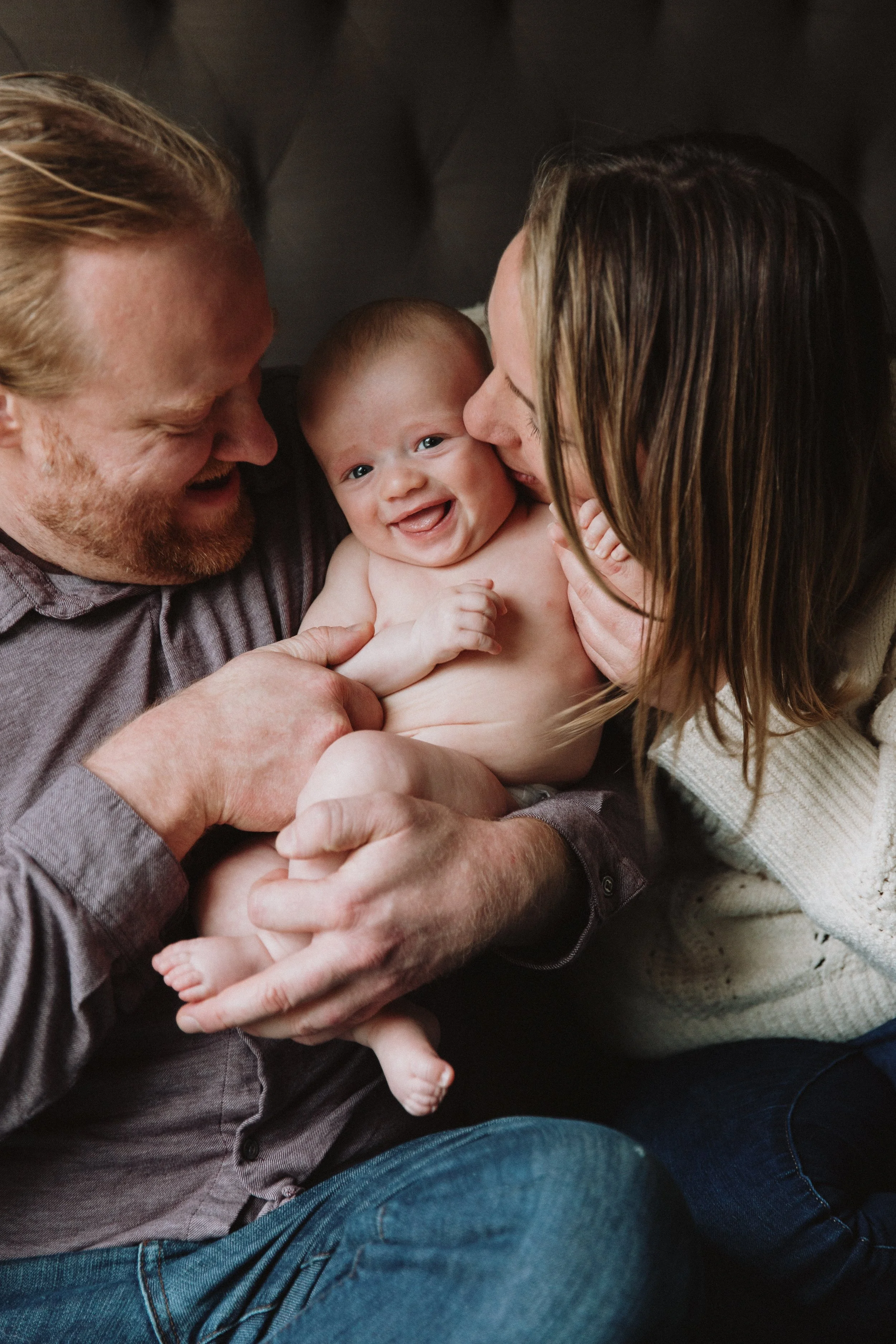 Smiling parents cuddling their laughing baby during an in-home newborn session