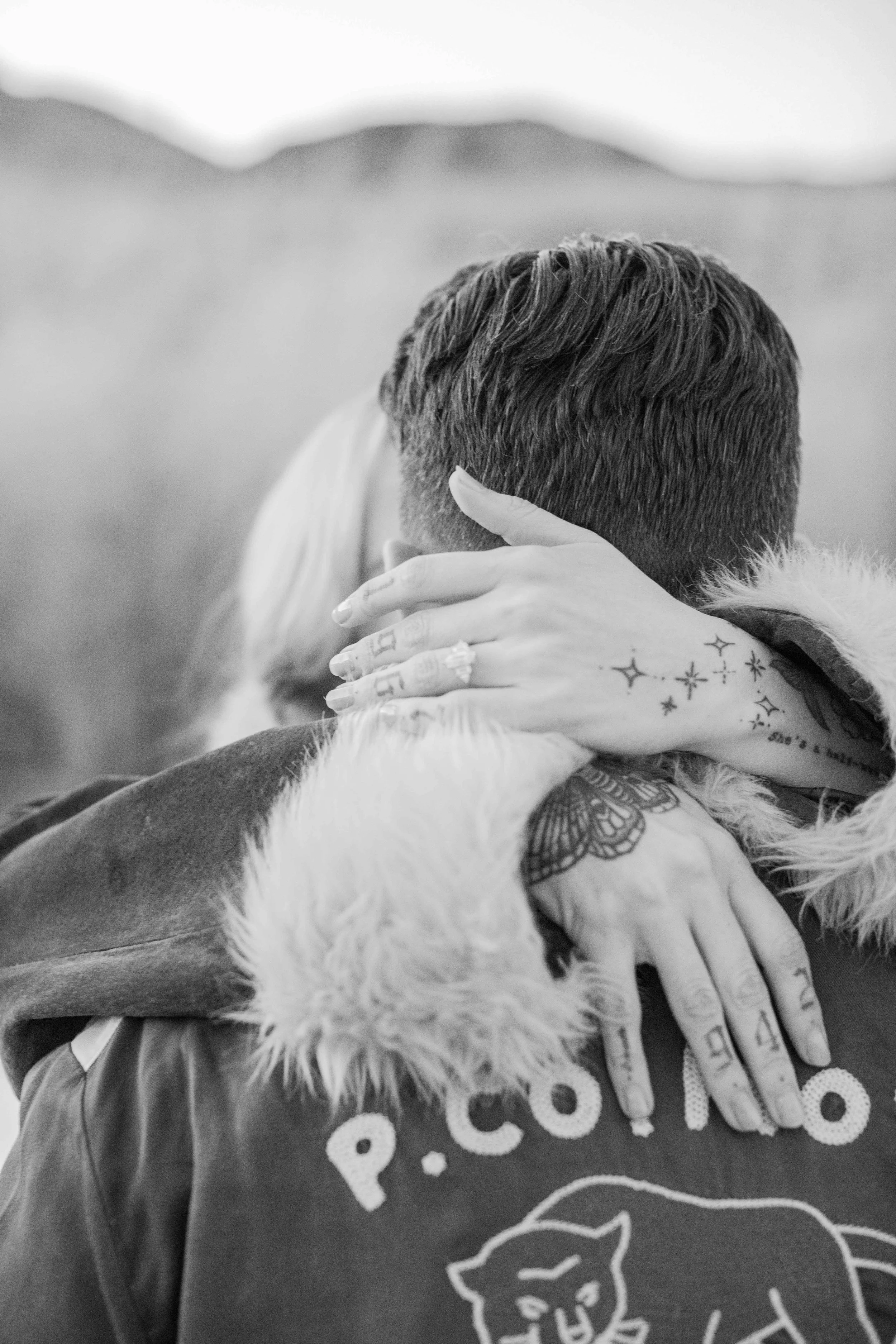 Black-and-white photo of a couple hugging after a proposal, the engagement ring on her hand