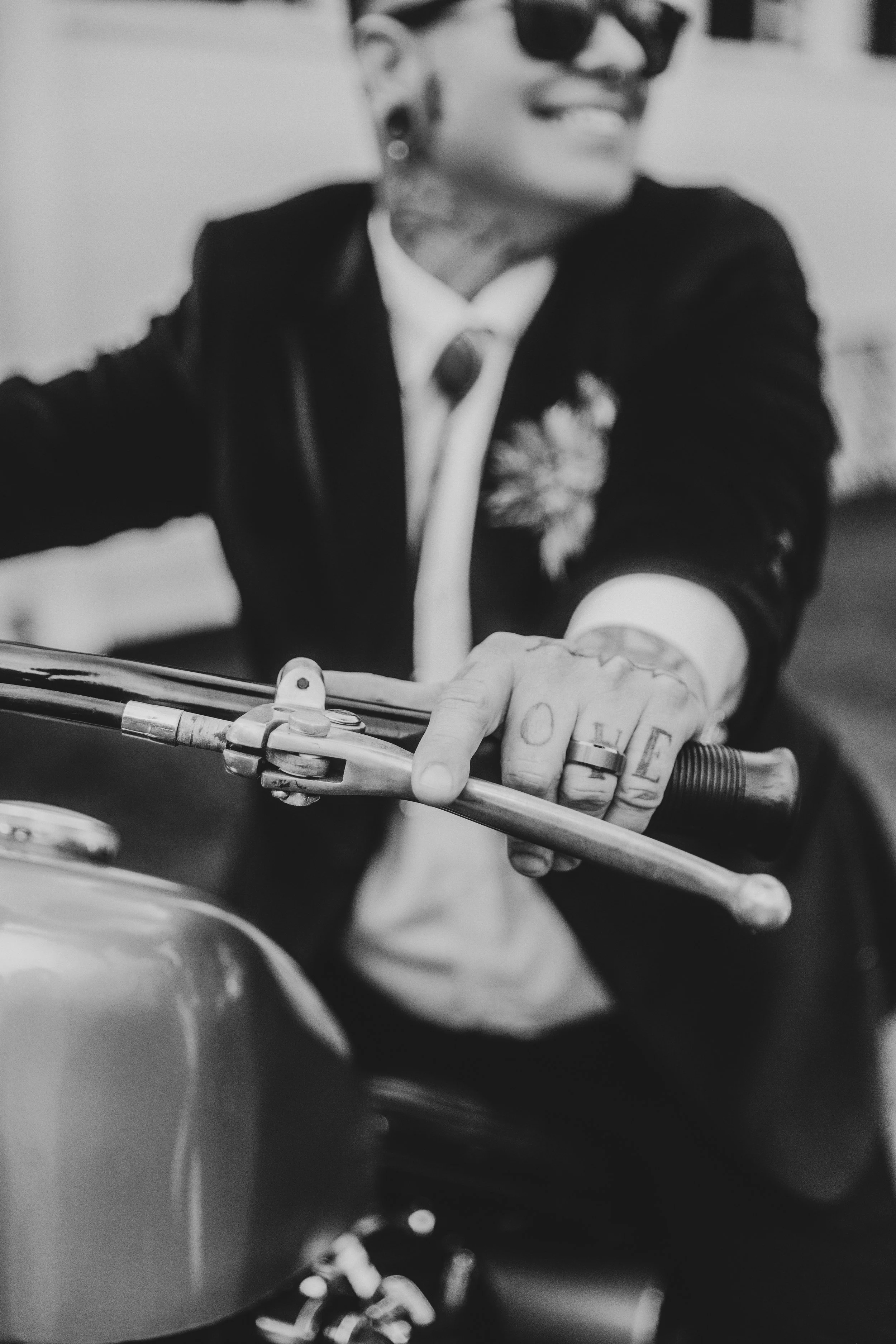 Black and white photo of a newlywed in a suit smiling on a motorcycle