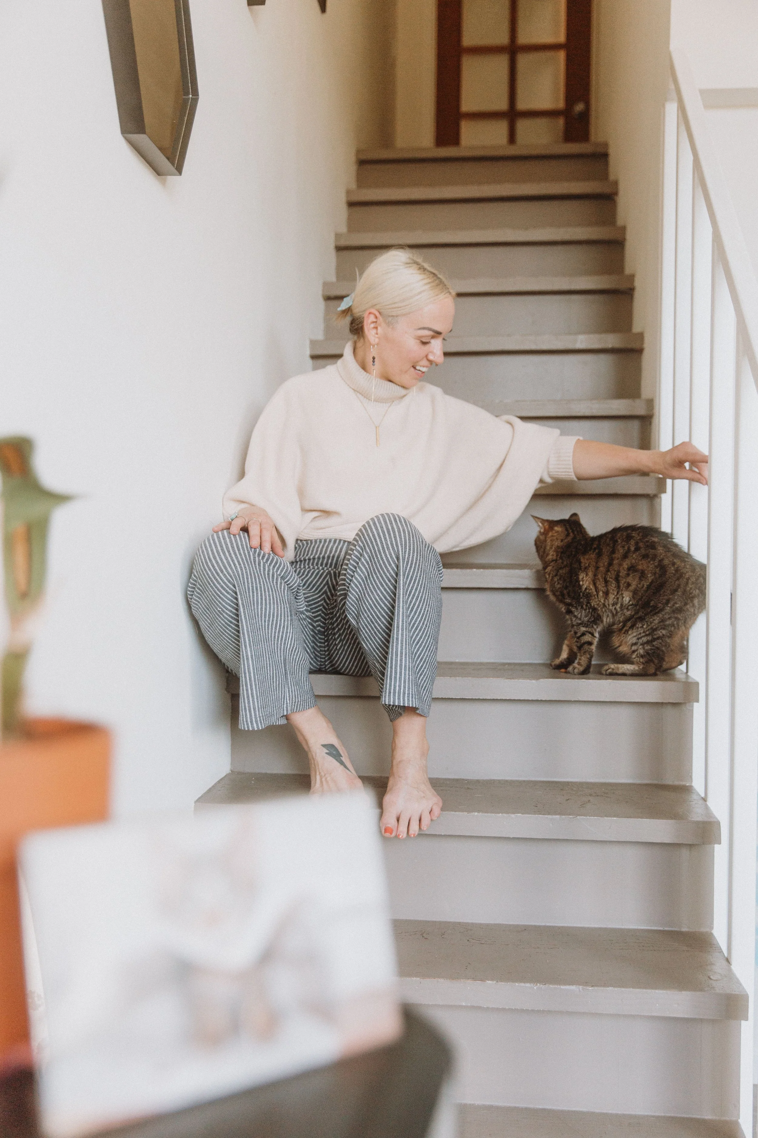 Woman petting her tabby cat on a sunlit staircase at home