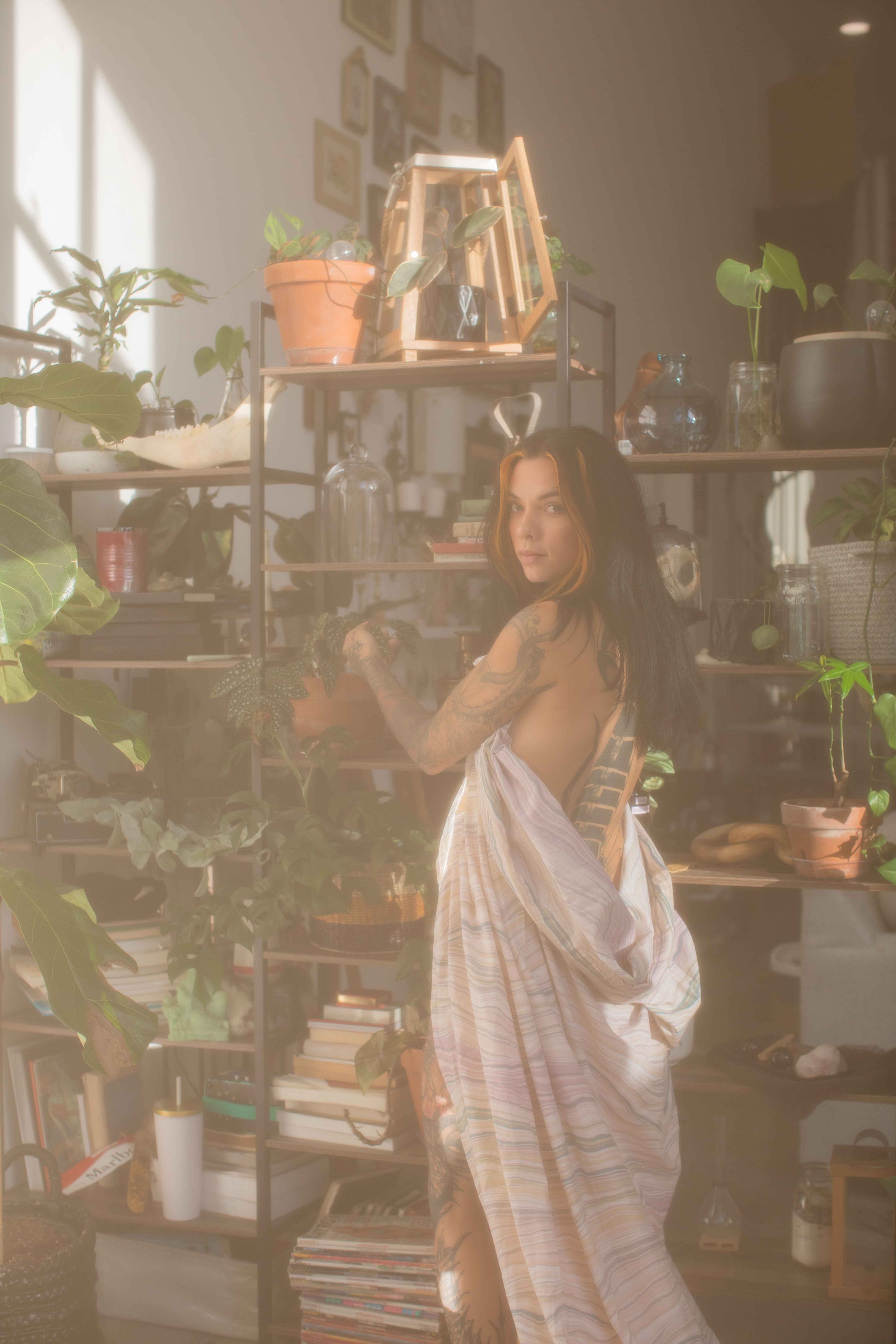Woman in a flowing dress among houseplants in a light-filled lifestyle portrait