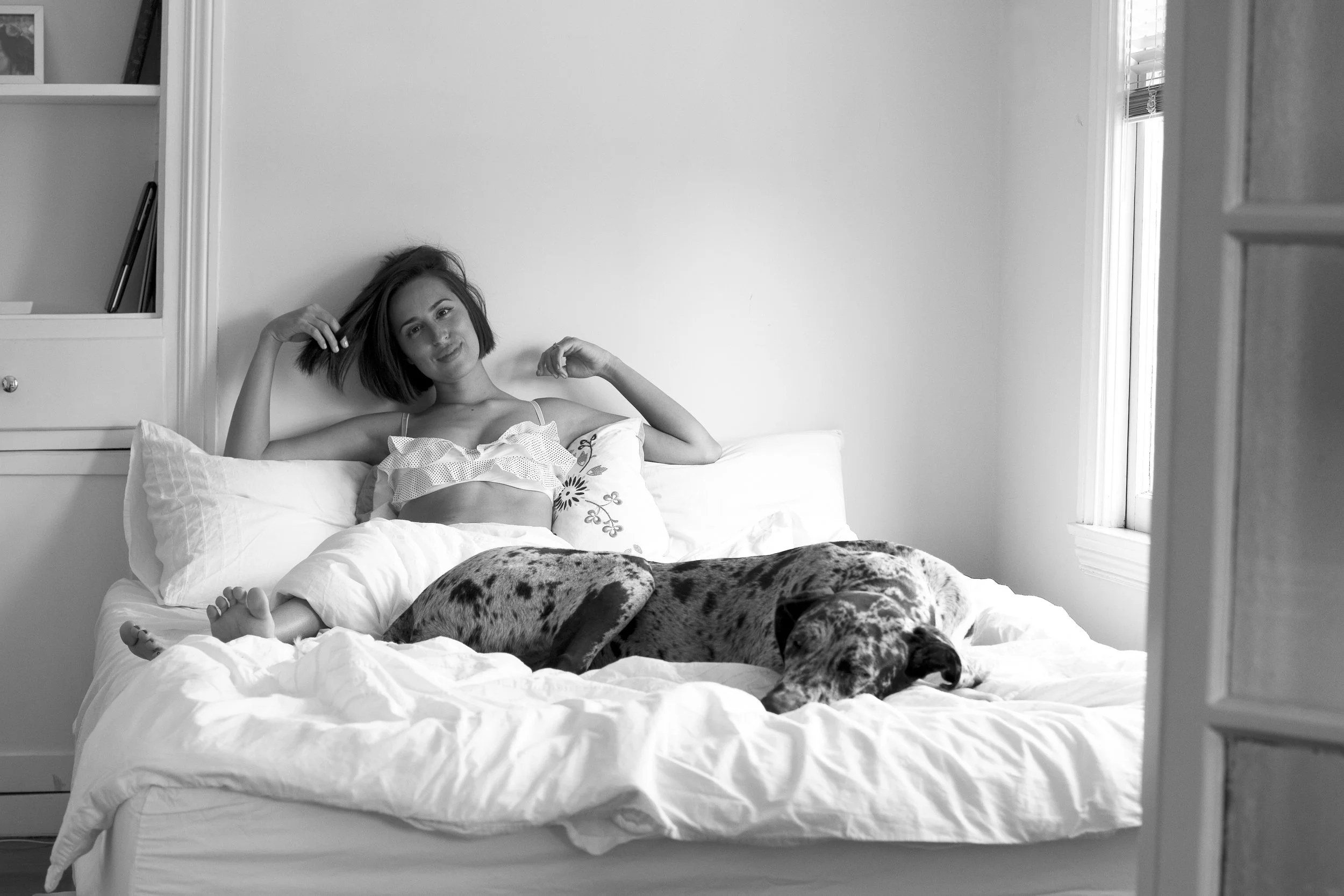 Woman relaxing in bed with her Great Dane in a black and white at-home portrait