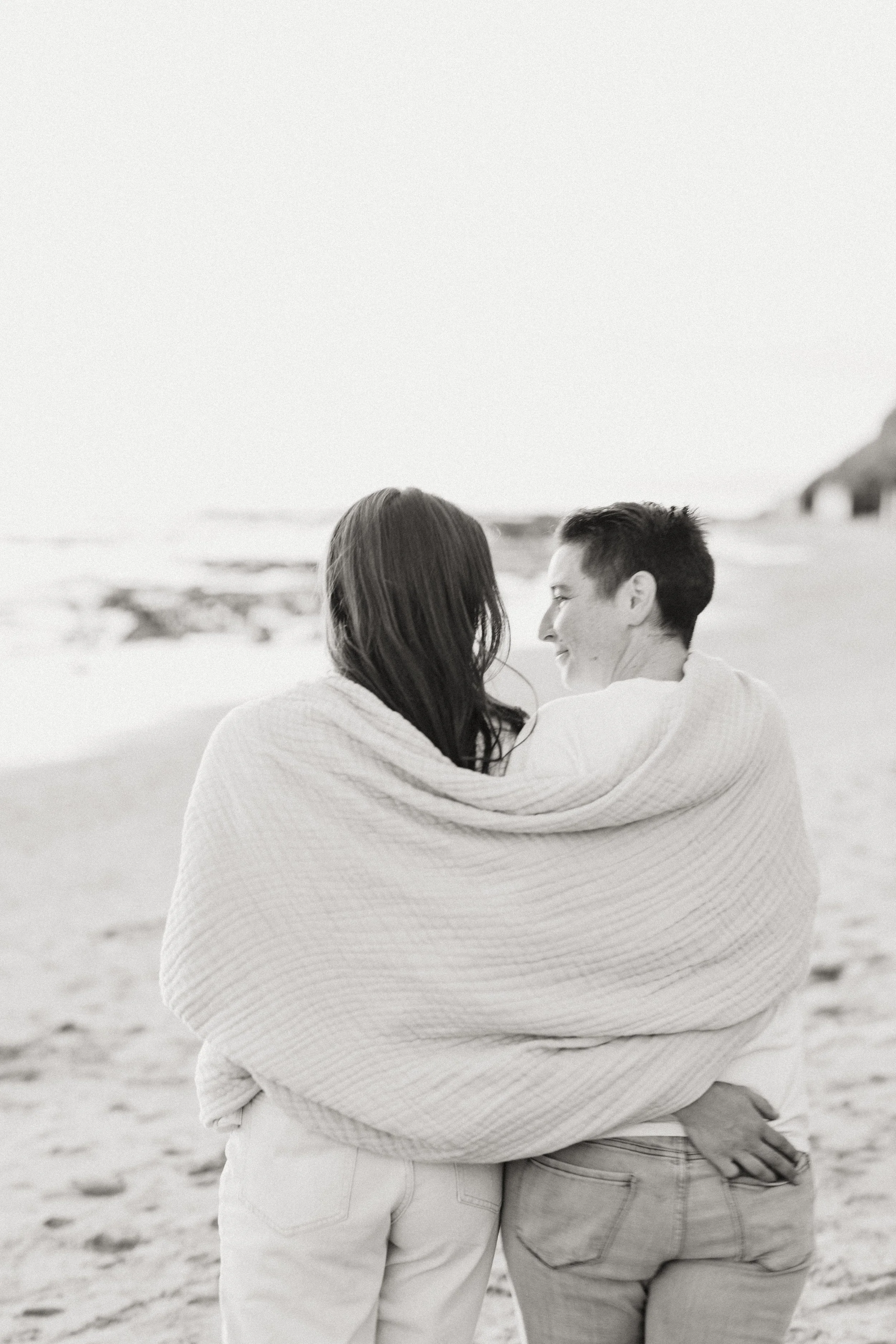 Couple wrapped in a blanket facing the ocean on the beach