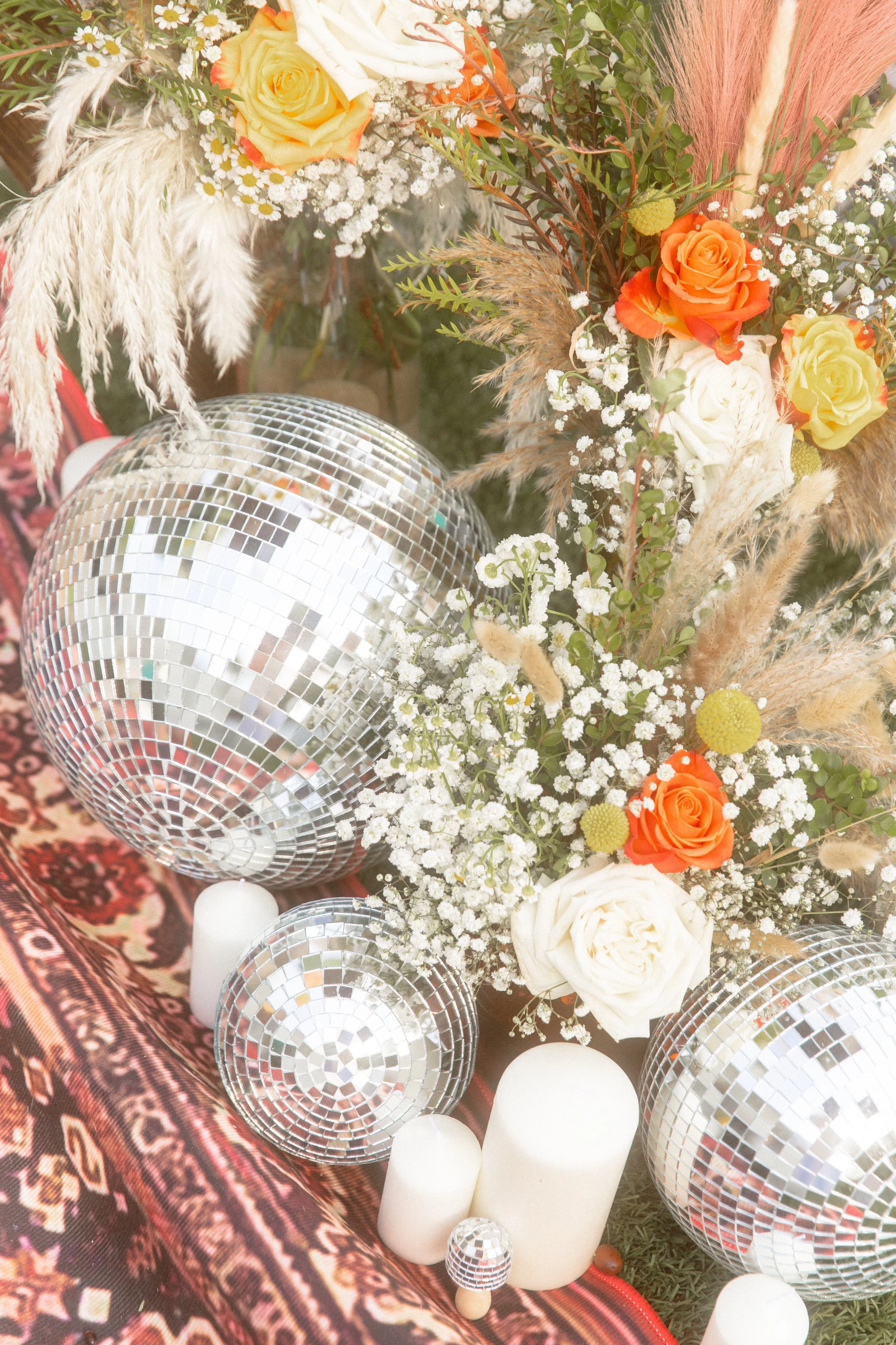 Disco balls, candles and orange and white flowers on a patterned rug at a wedding ceremony