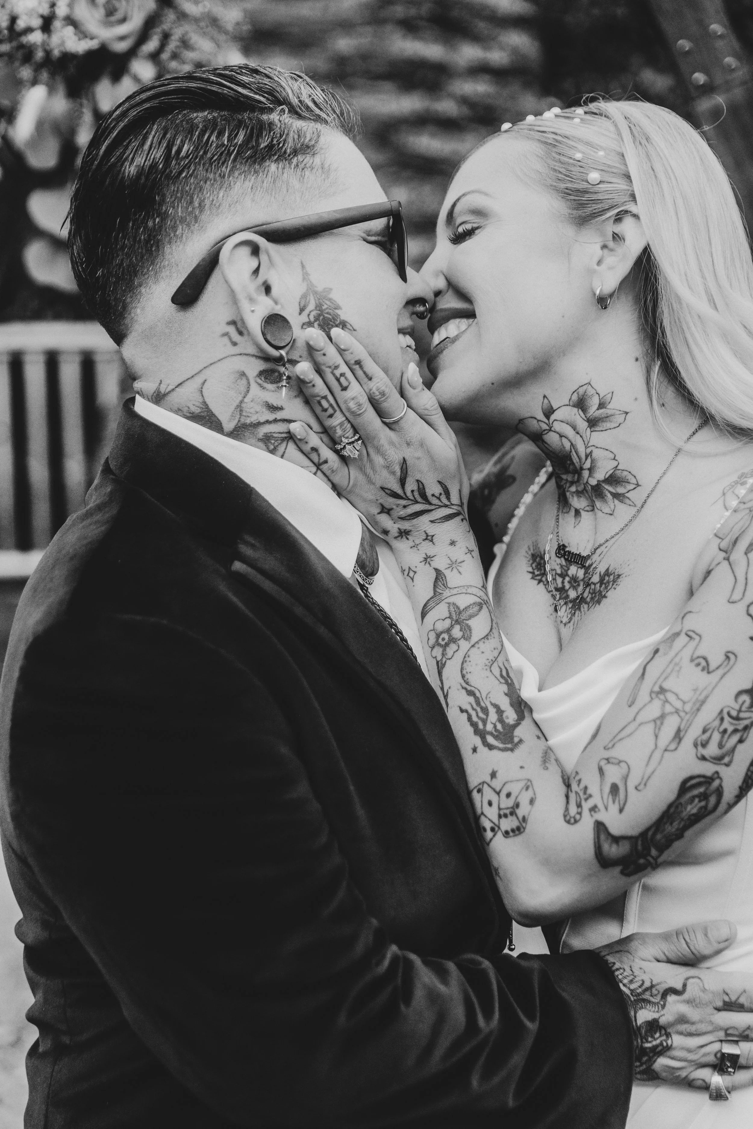 Black and white photo of newlyweds about to kiss, a tattooed hand on a cheek
