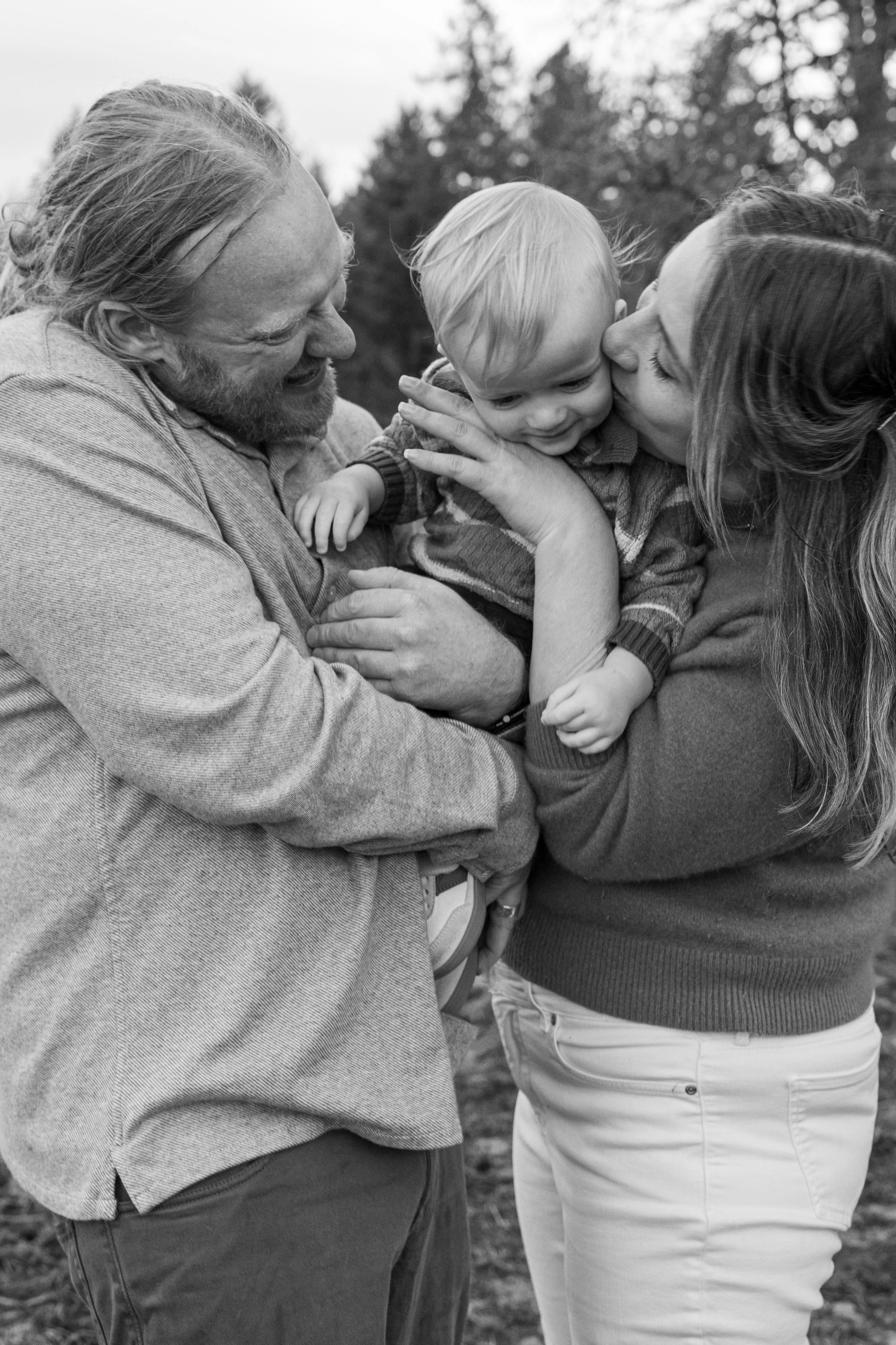 Black-and-white photo of parents kissing their laughing toddler during a family session