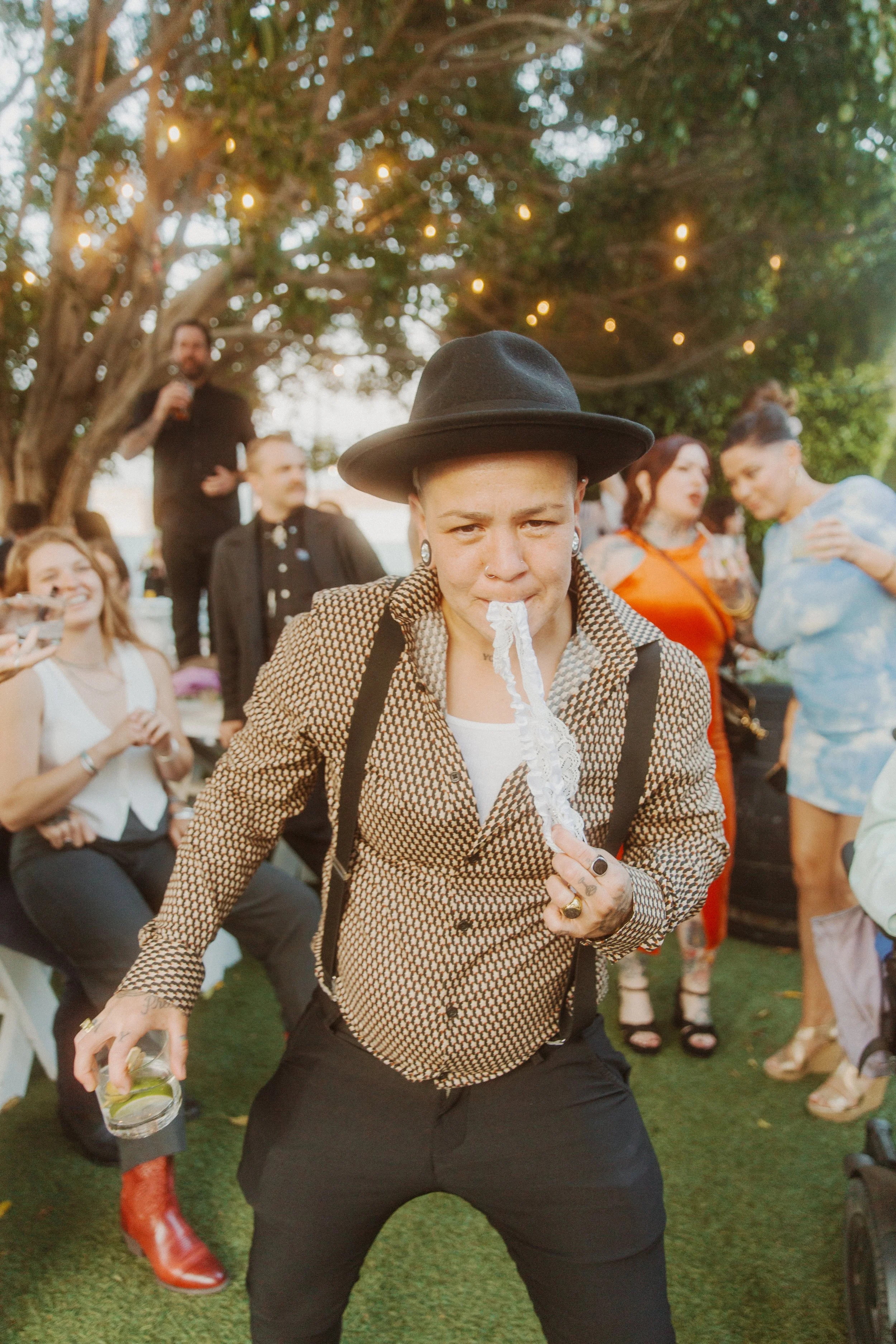 Wedding guest in a hat and suspenders dancing with a drink in hand