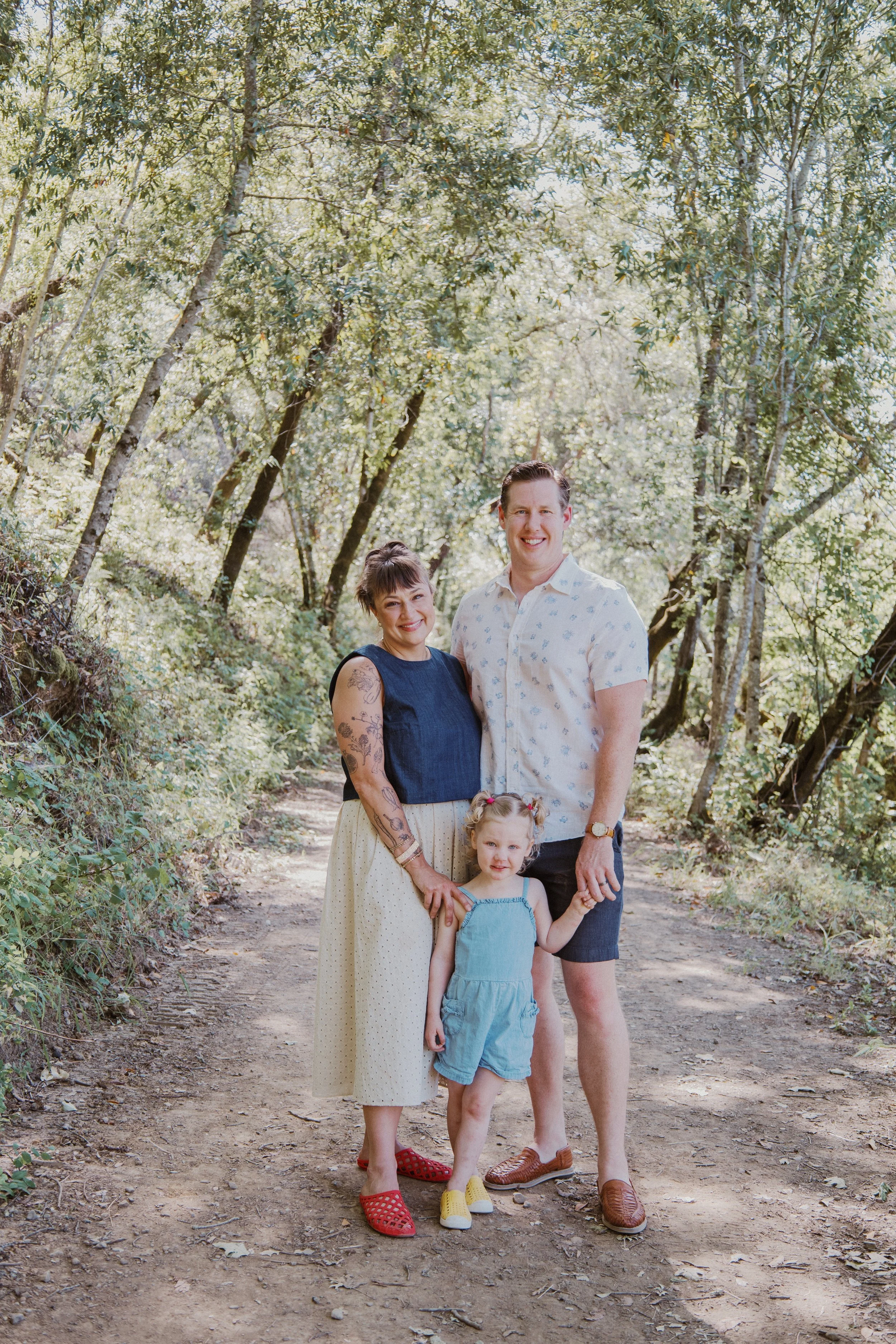 Family of three standing together on a tree-lined trail