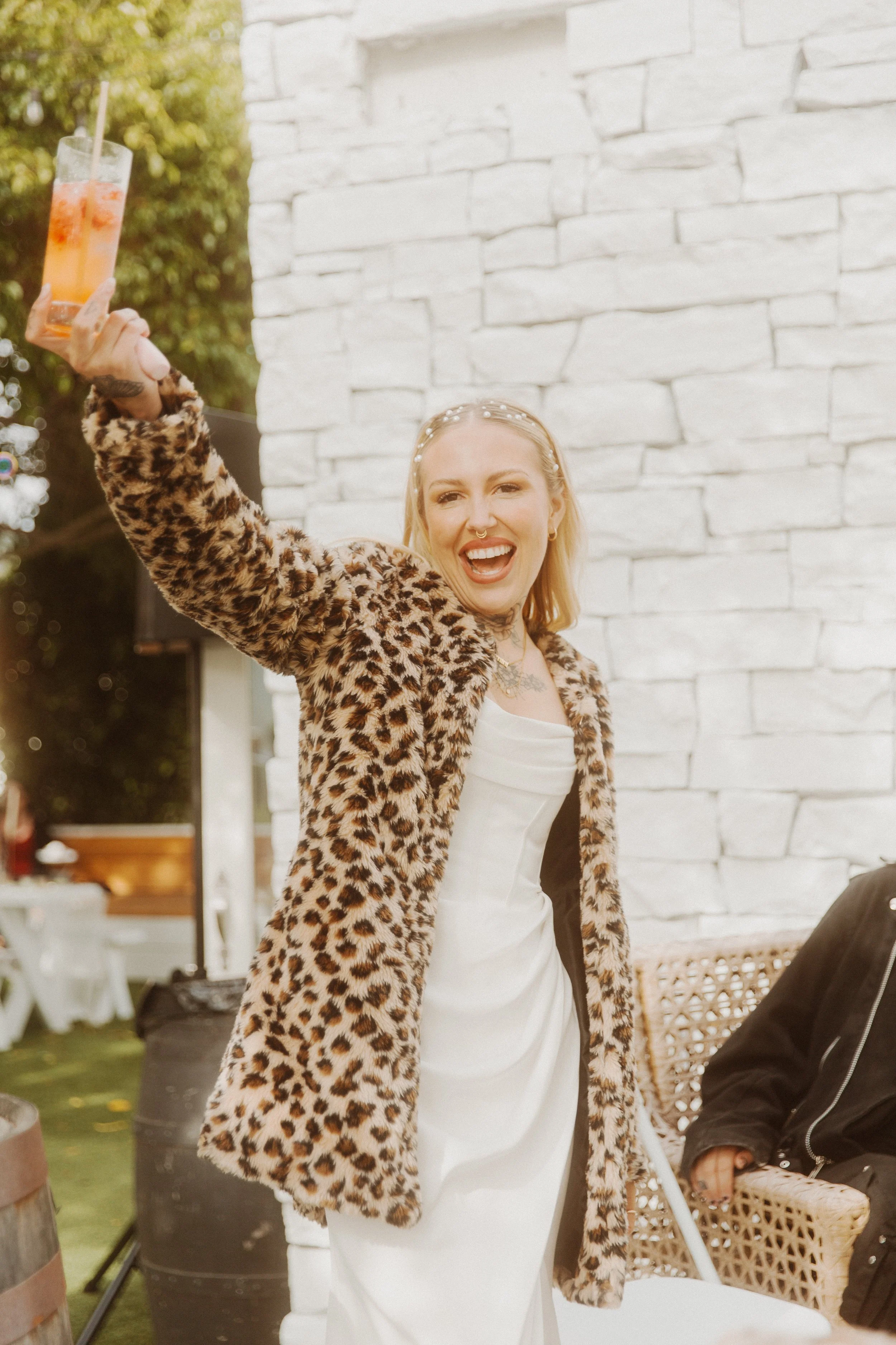 Bride in a leopard print coat raising a drink in a toast