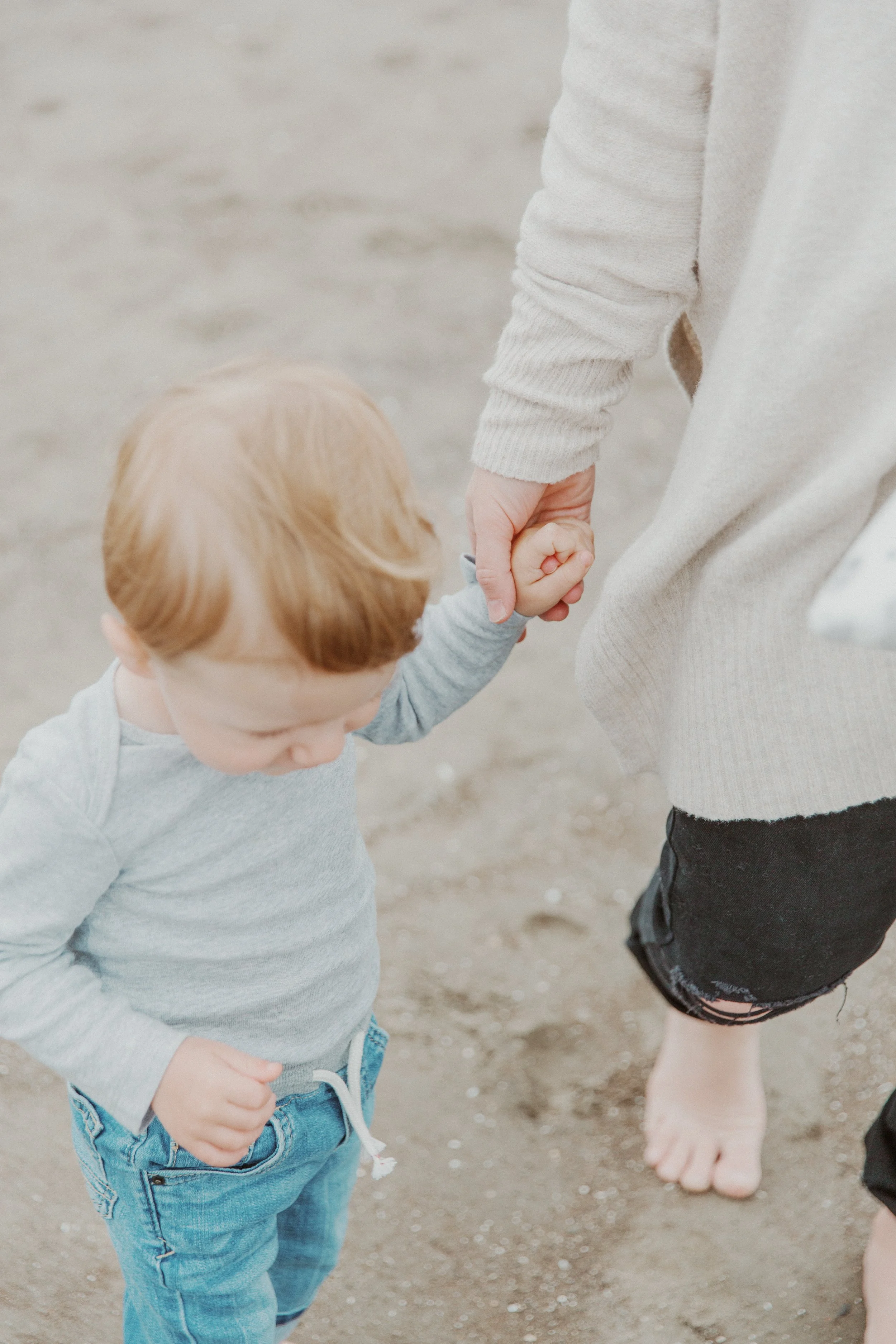 Toddler holding a parent's hand while walking on the beach