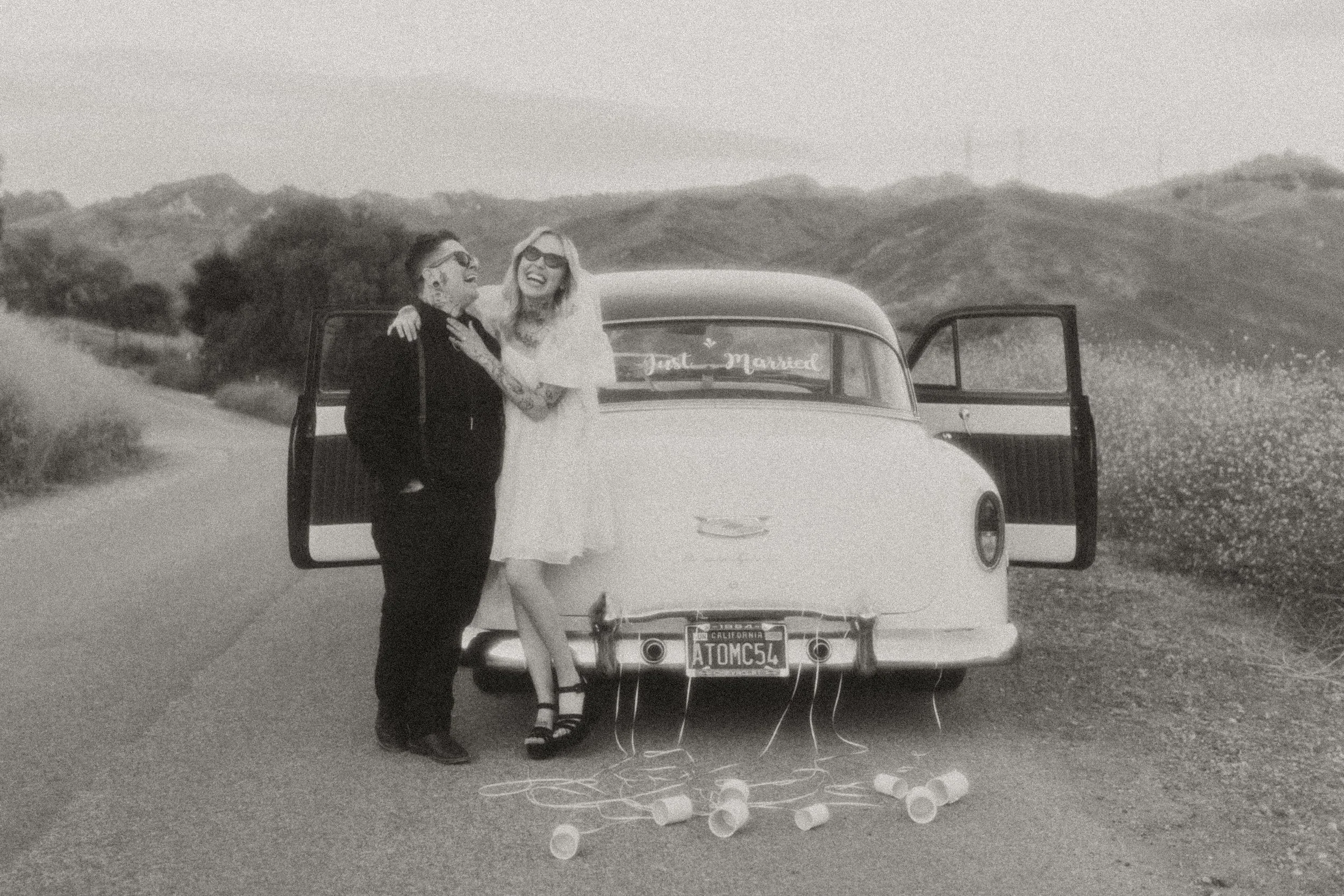 Black and white photo of newlyweds kissing beside a vintage car