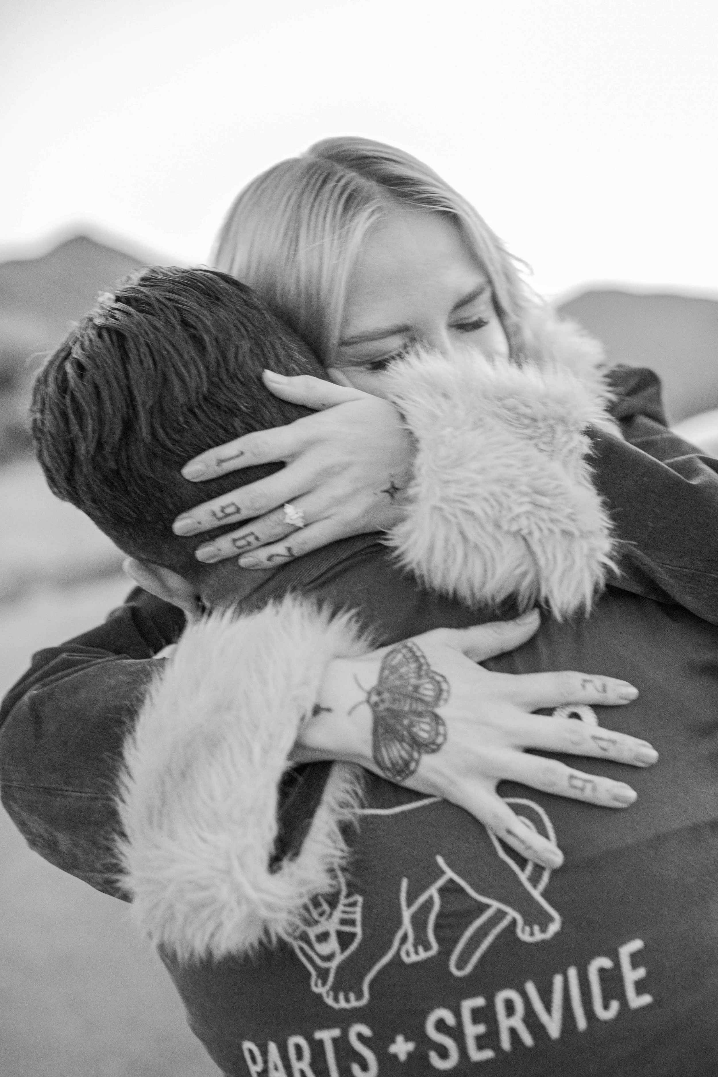 Black and white photo of a couple hugging right after a hillside proposal