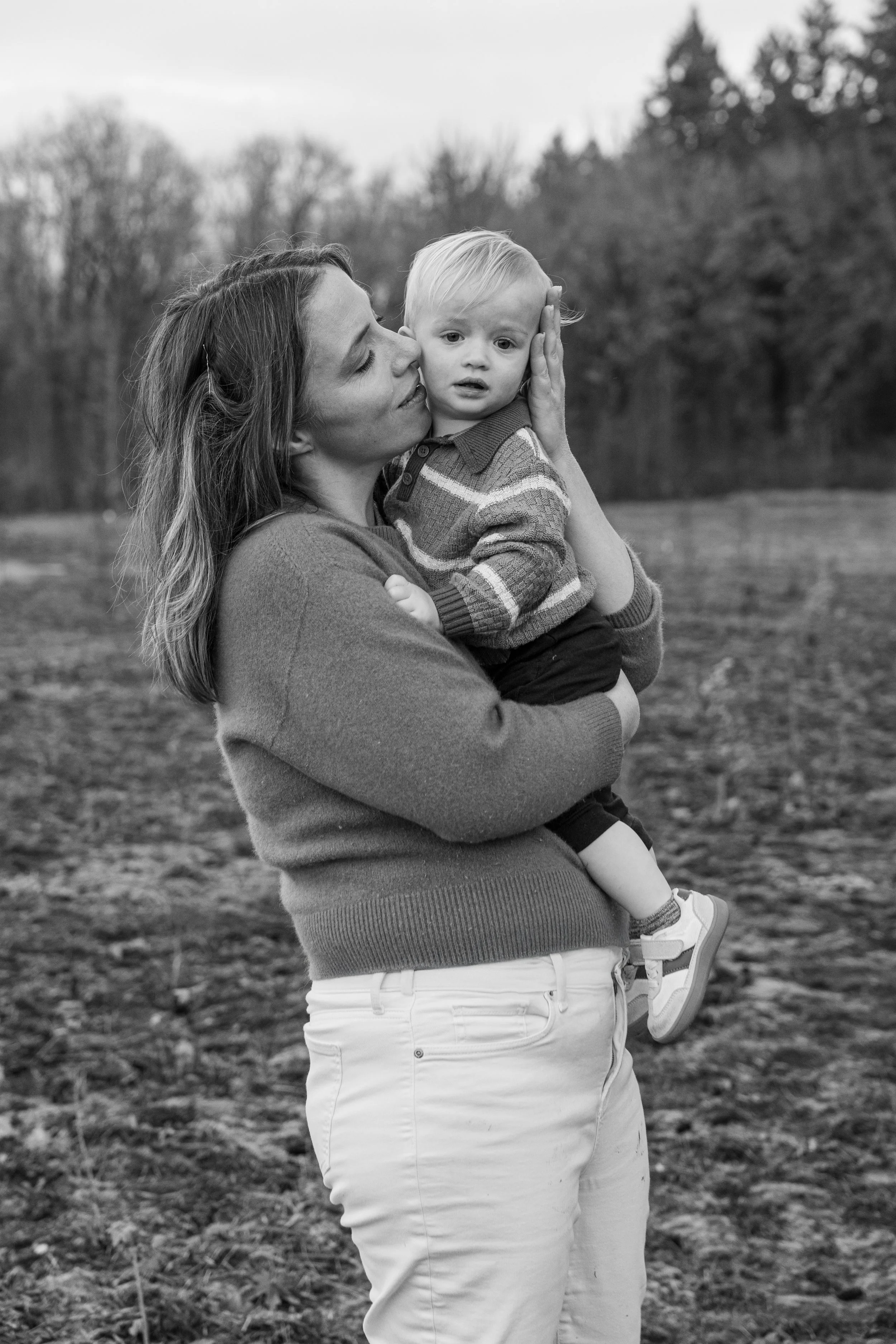 Black and white photo of a mother holding her toddler in an open field
