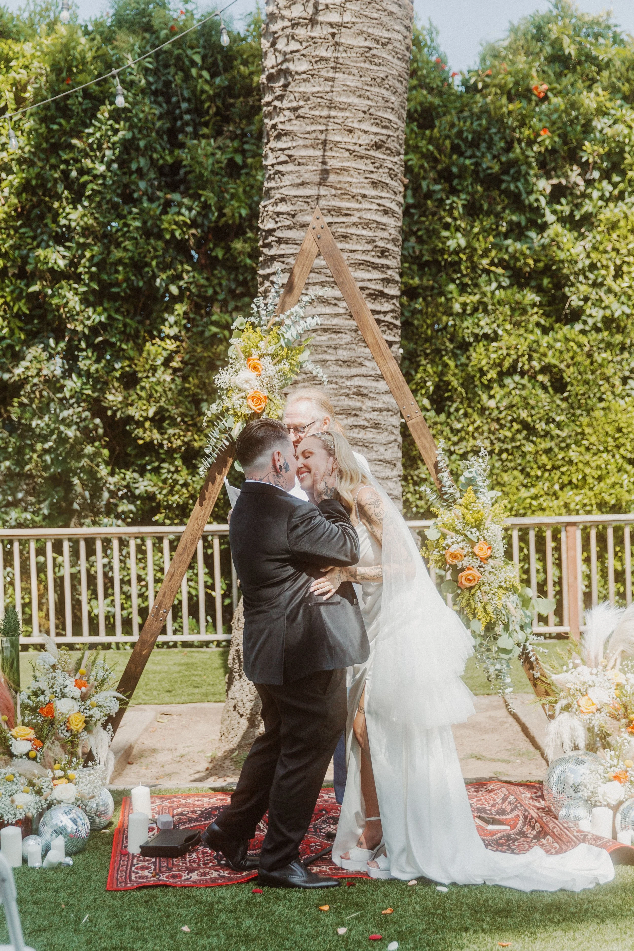Newlyweds sharing their first kiss under a wooden arch by a palm tree