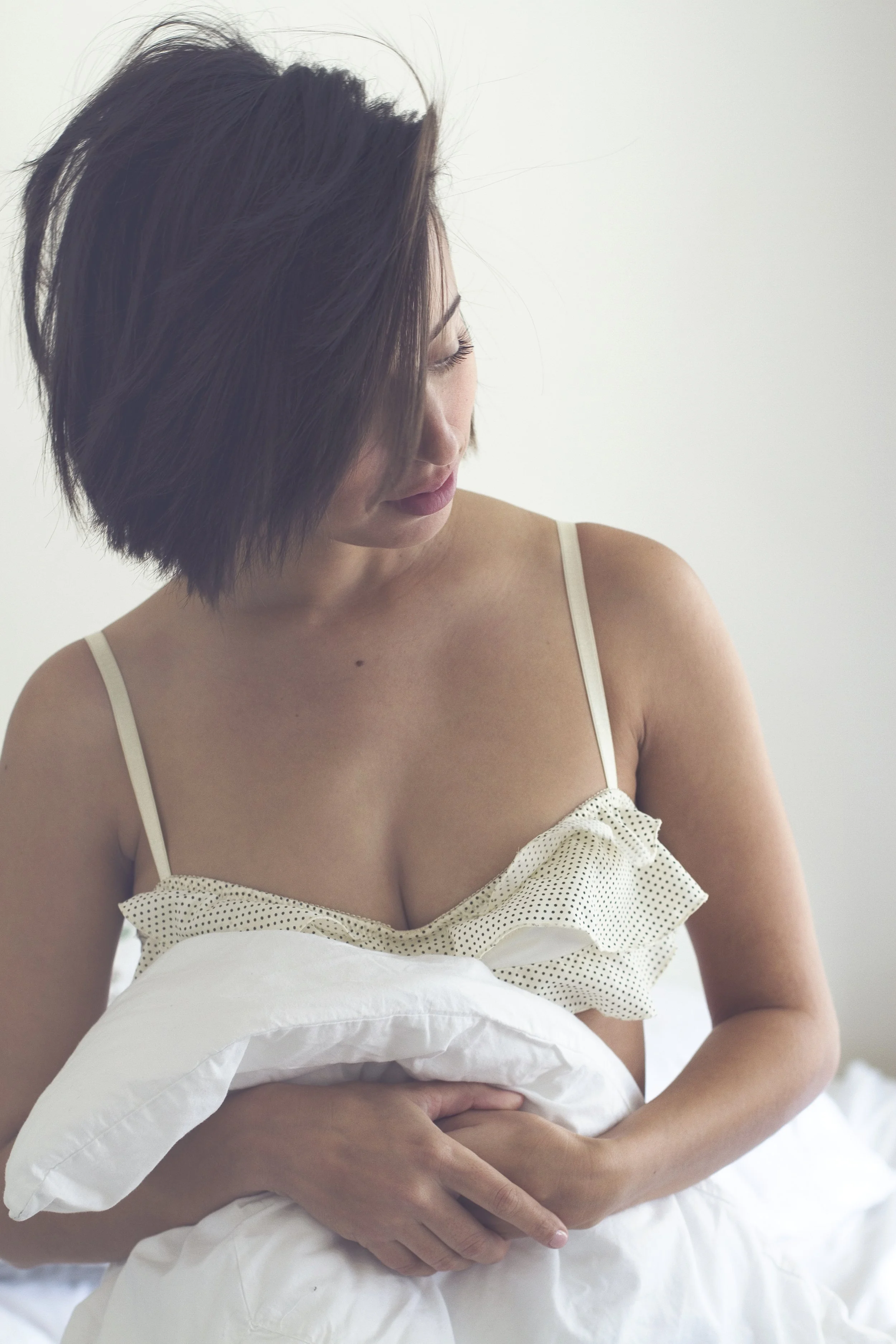 Woman hugging a white pillow in a soft, intimate at-home portrait