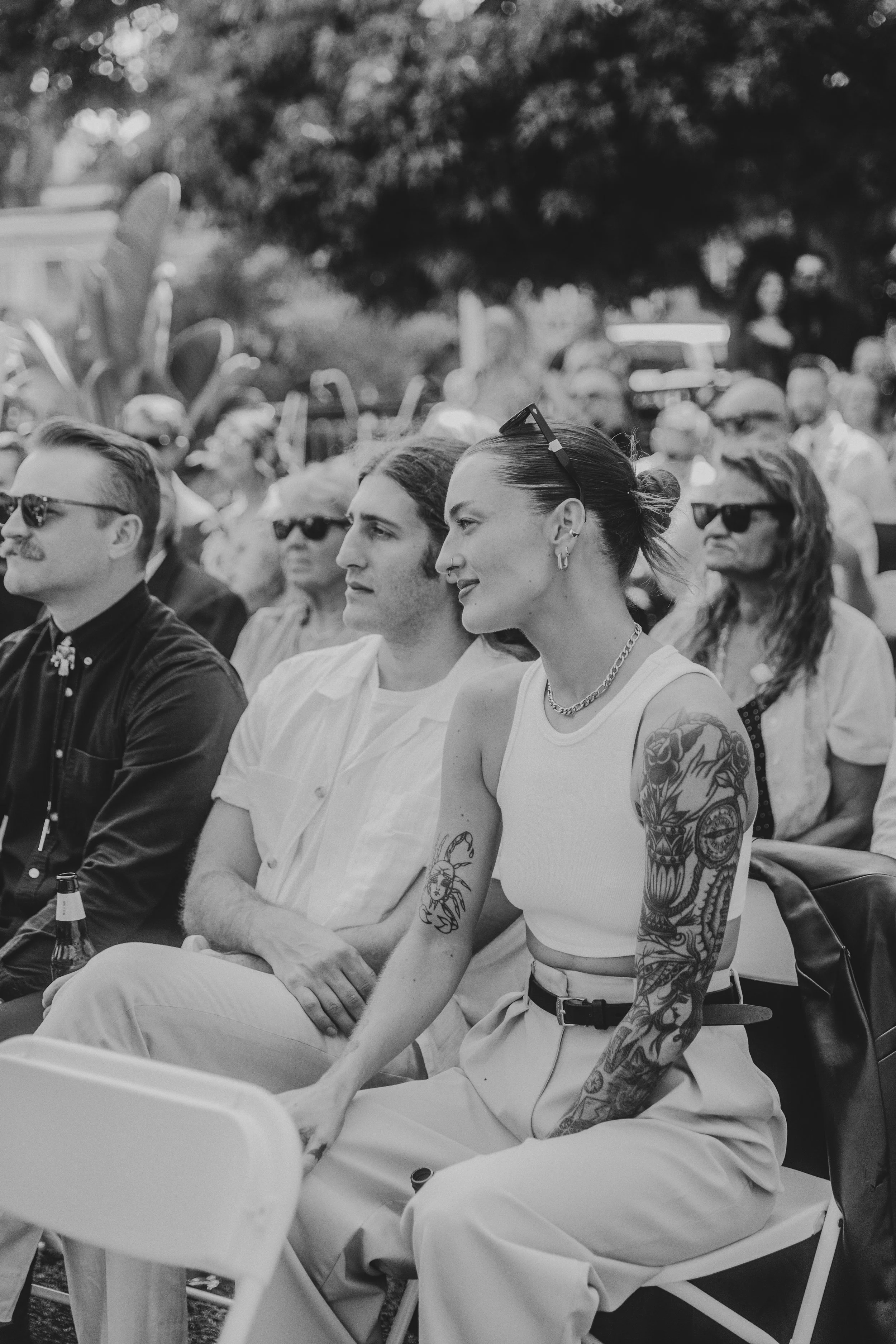 Black and white photo of seated wedding guests in sunglasses watching the ceremony