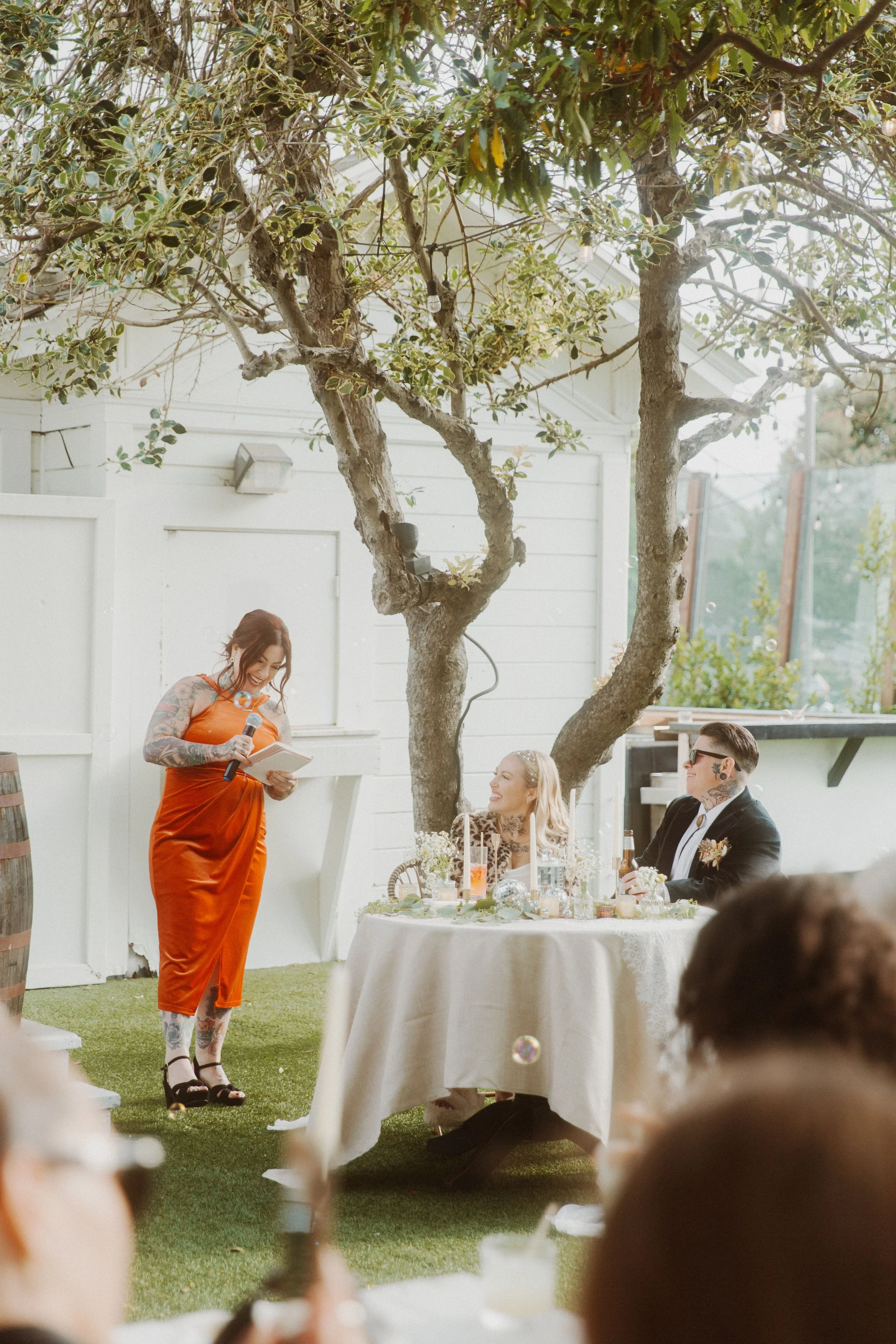 Guest in an orange dress giving a toast at a garden wedding reception