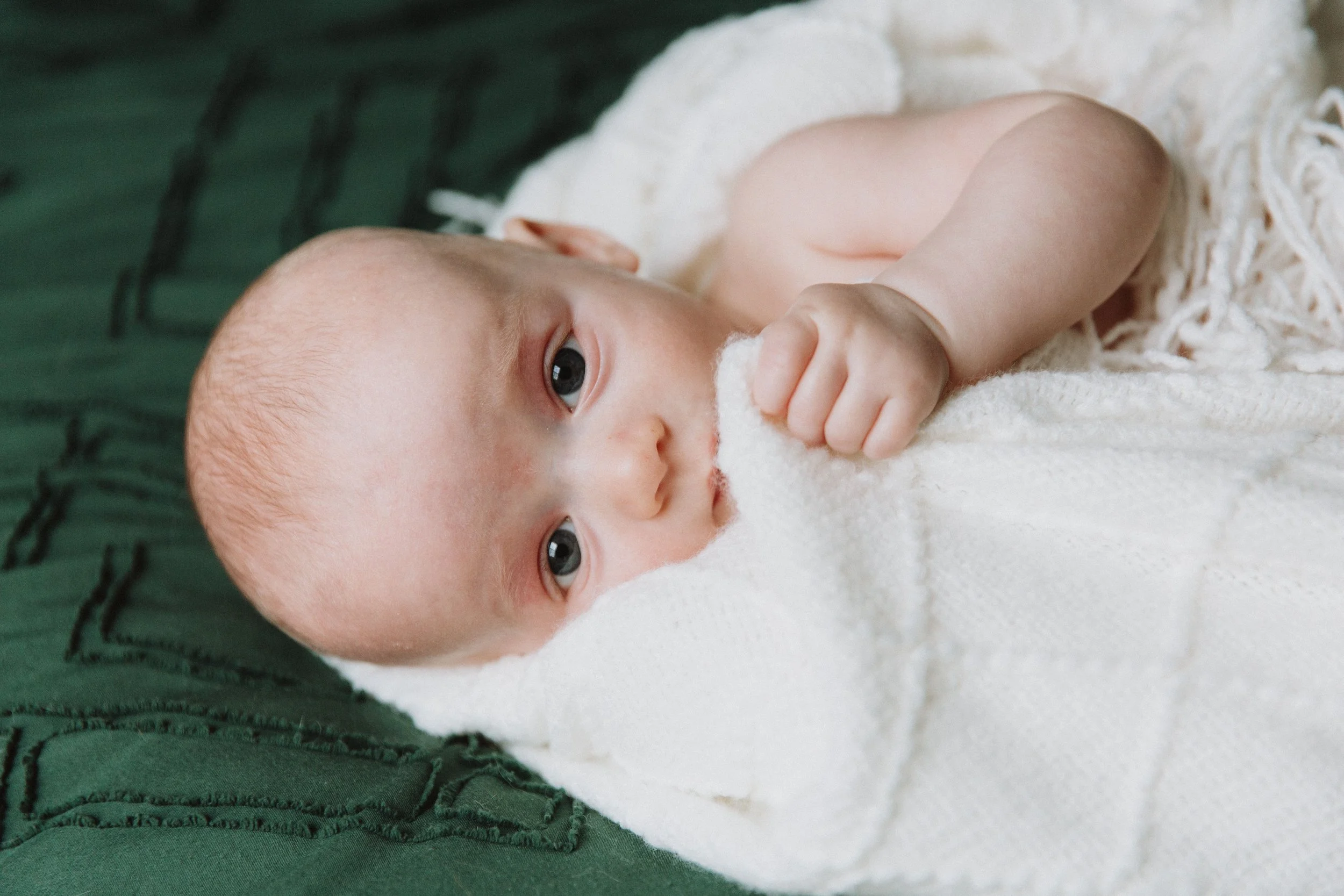 Baby lying on a cream blanket and looking up at the camera