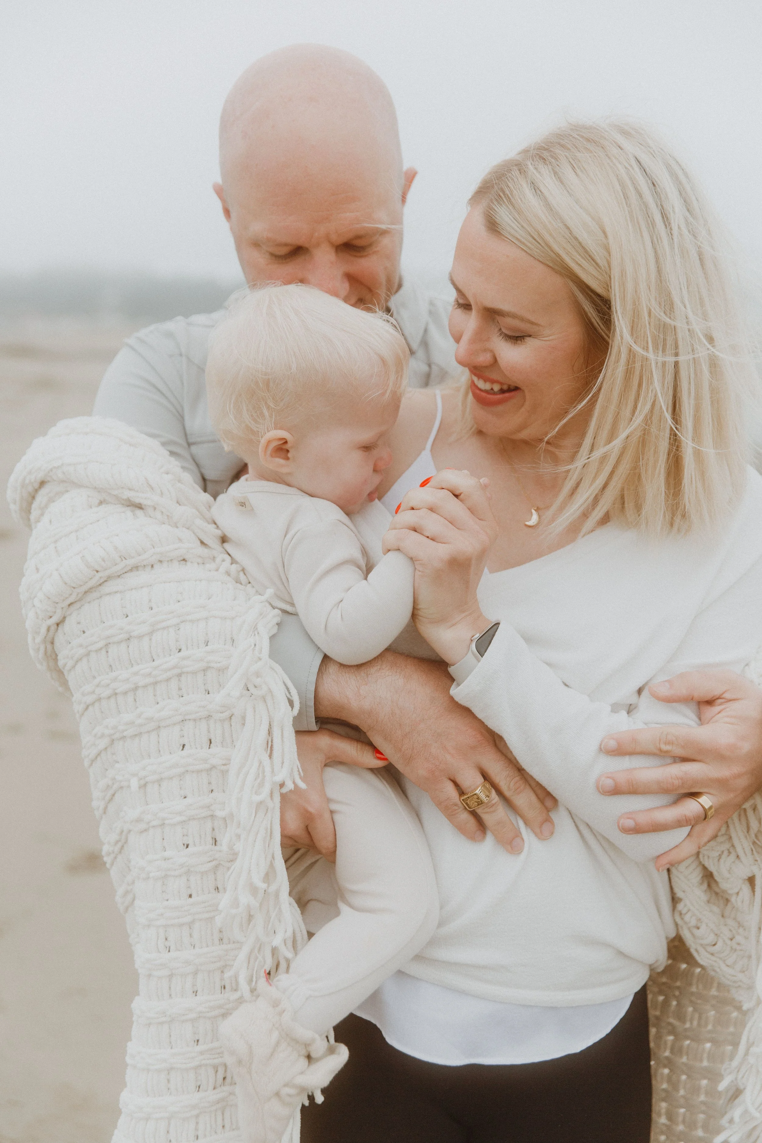Parents cuddling their baby together in a joyful beach family photo