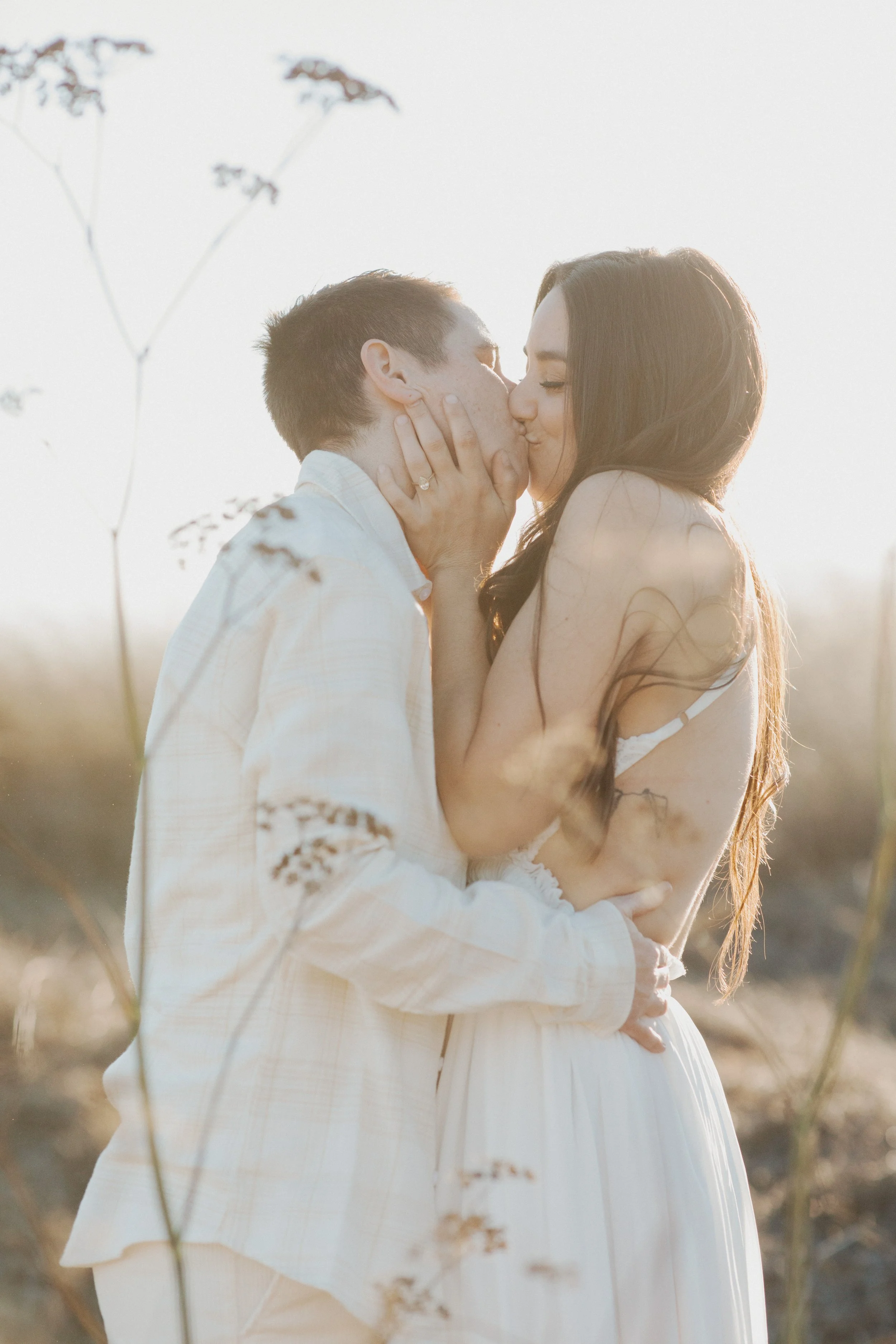 Couple kissing among tall grasses at sunset