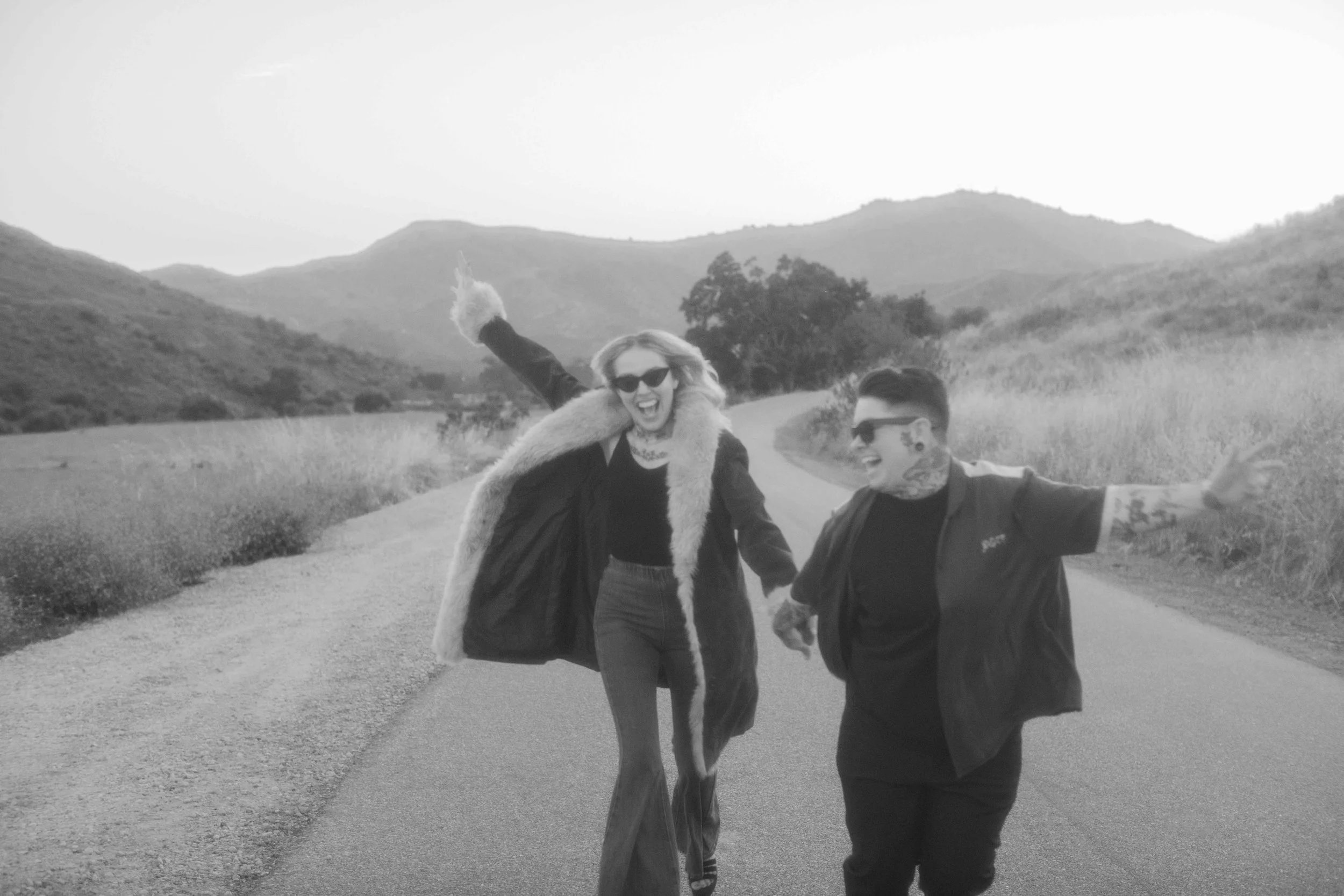 Black and white photo of a couple walking down a country road in the hills
