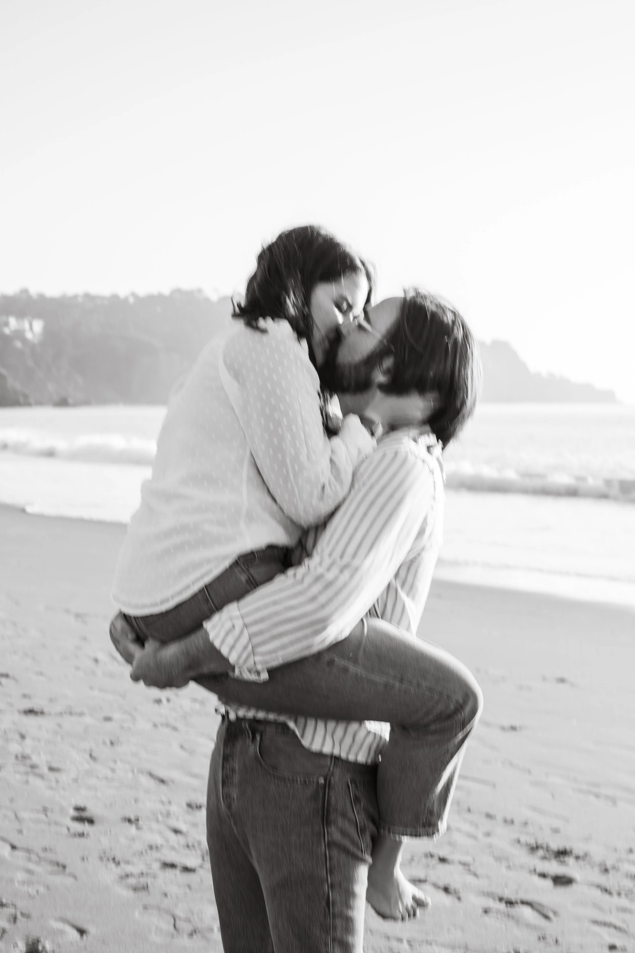 Couple hugging and laughing on the beach in a black and white engagement photo