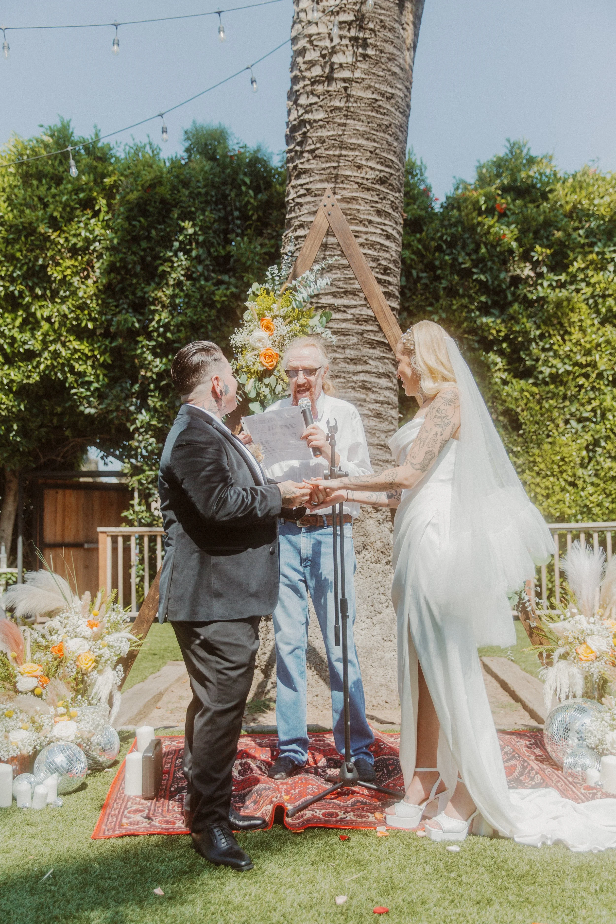 Couple exchanging vows with their officiant under a palm tree