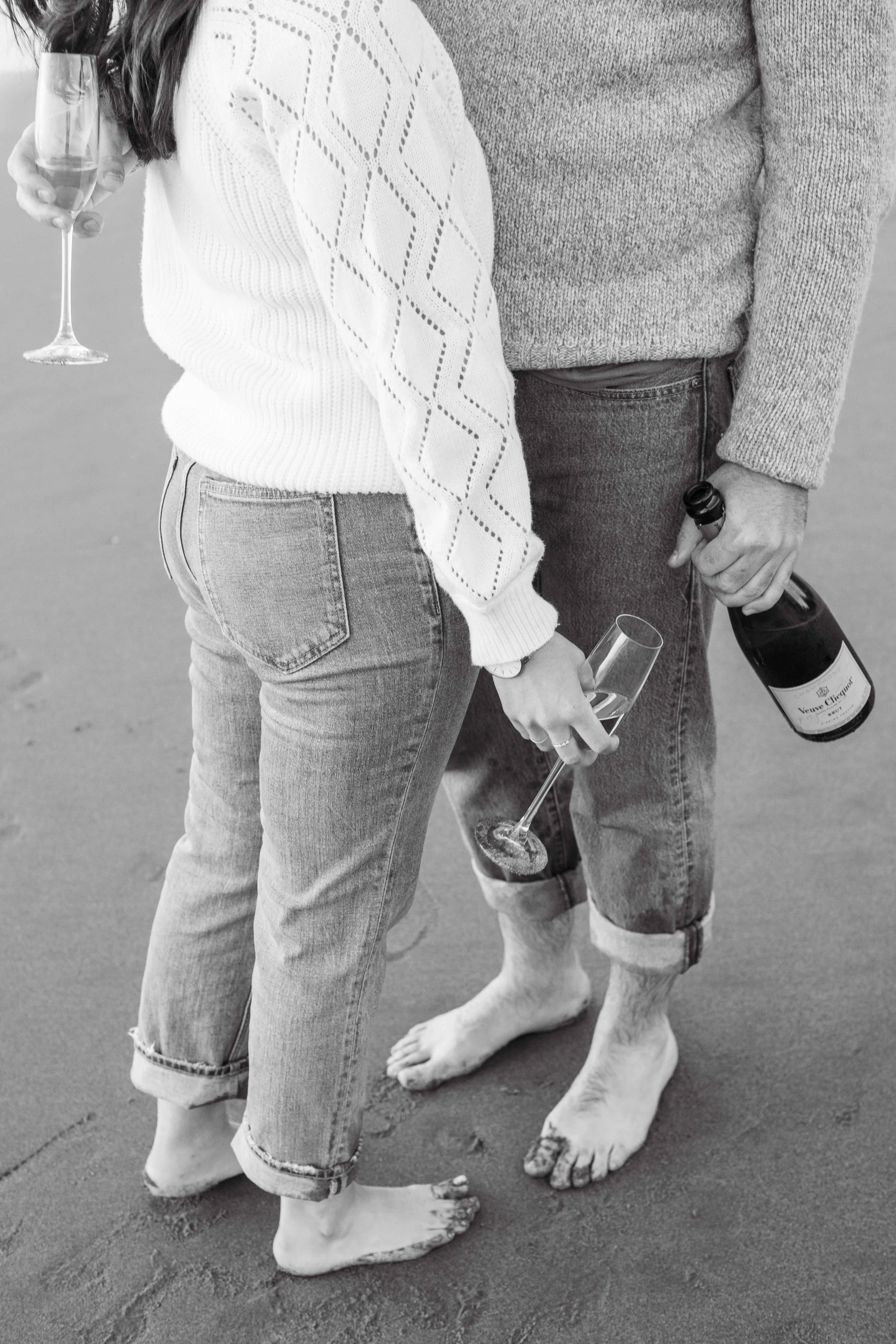 Black and white photo of a barefoot couple standing close on the beach