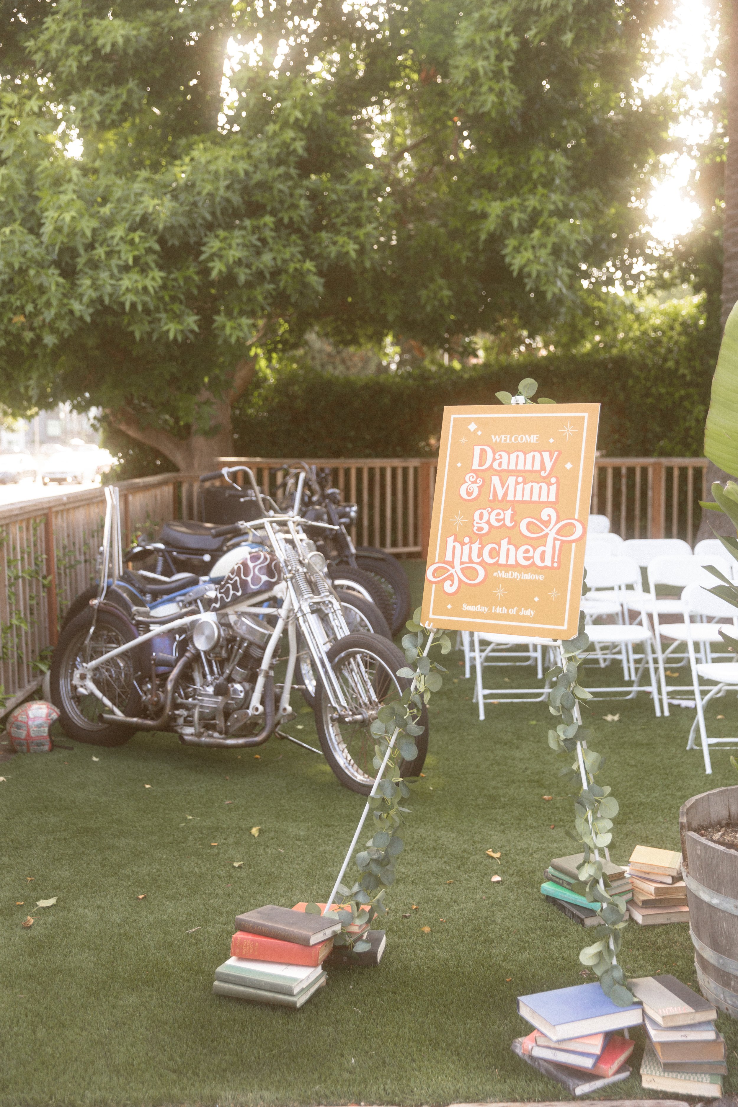 Welcome sign beside a vintage bicycle and stacked books at a backyard wedding