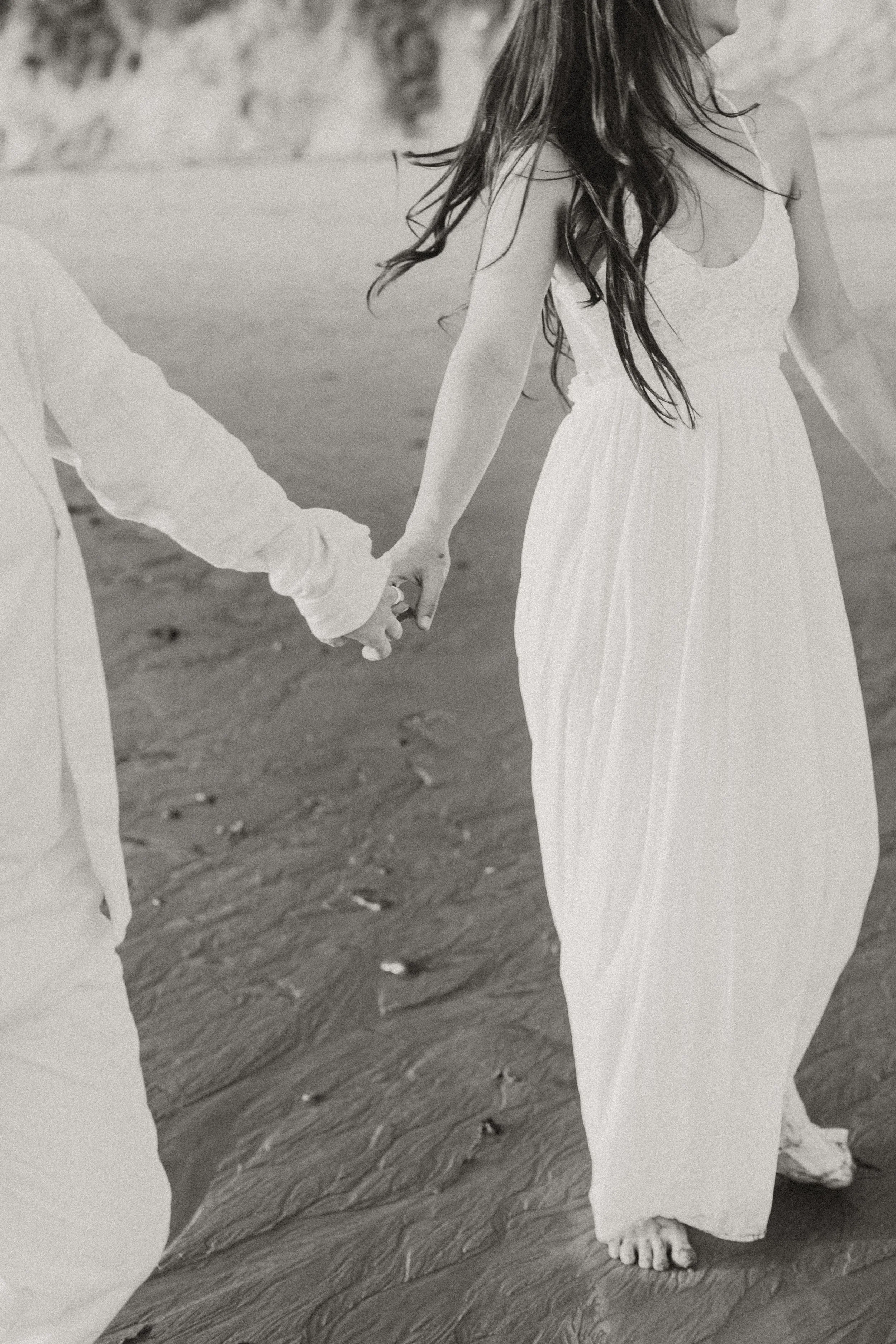 Black and white photo of a couple walking hand in hand on the beach