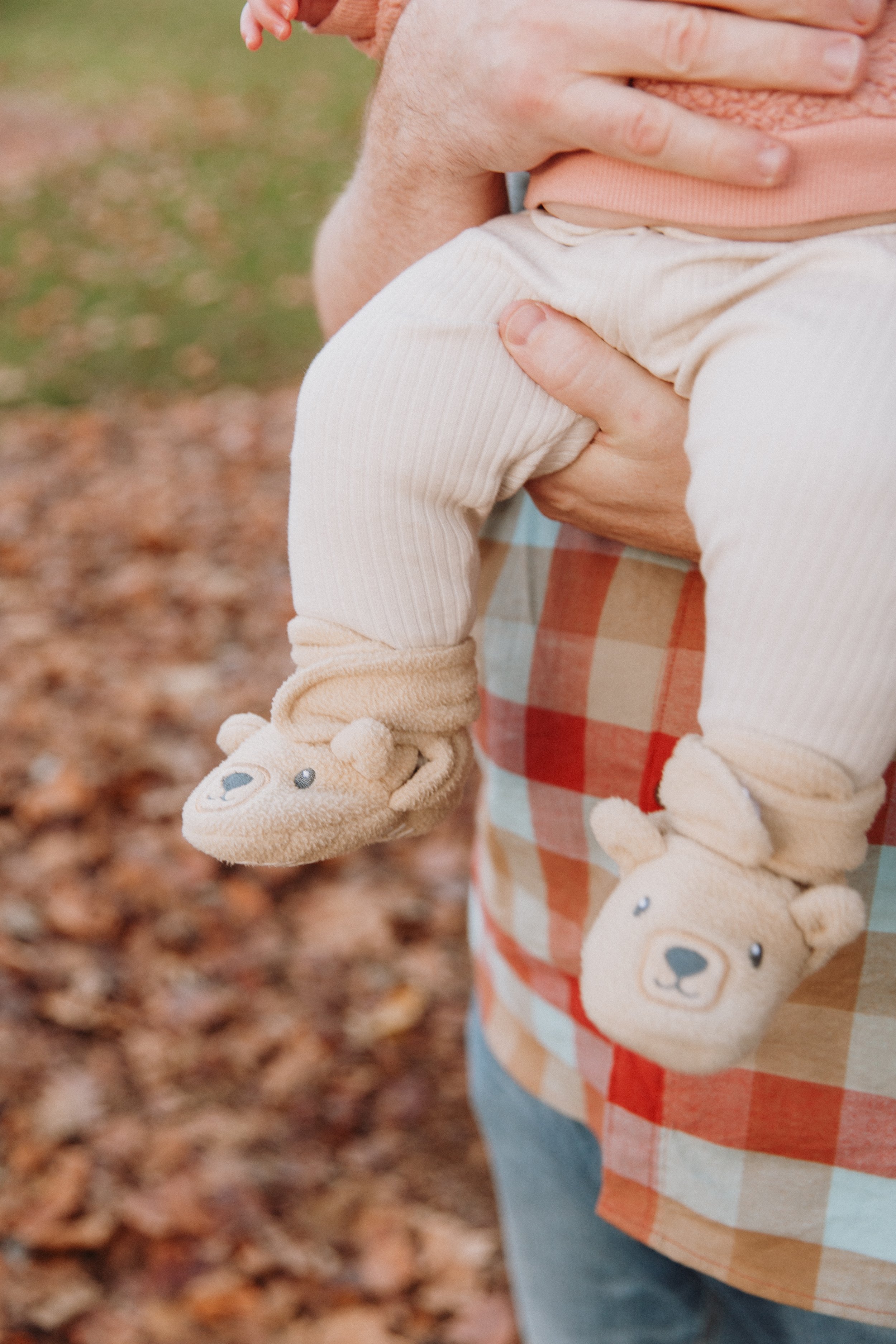 Baby's fuzzy bear booties against dad's plaid shirt in a park full of fall leaves