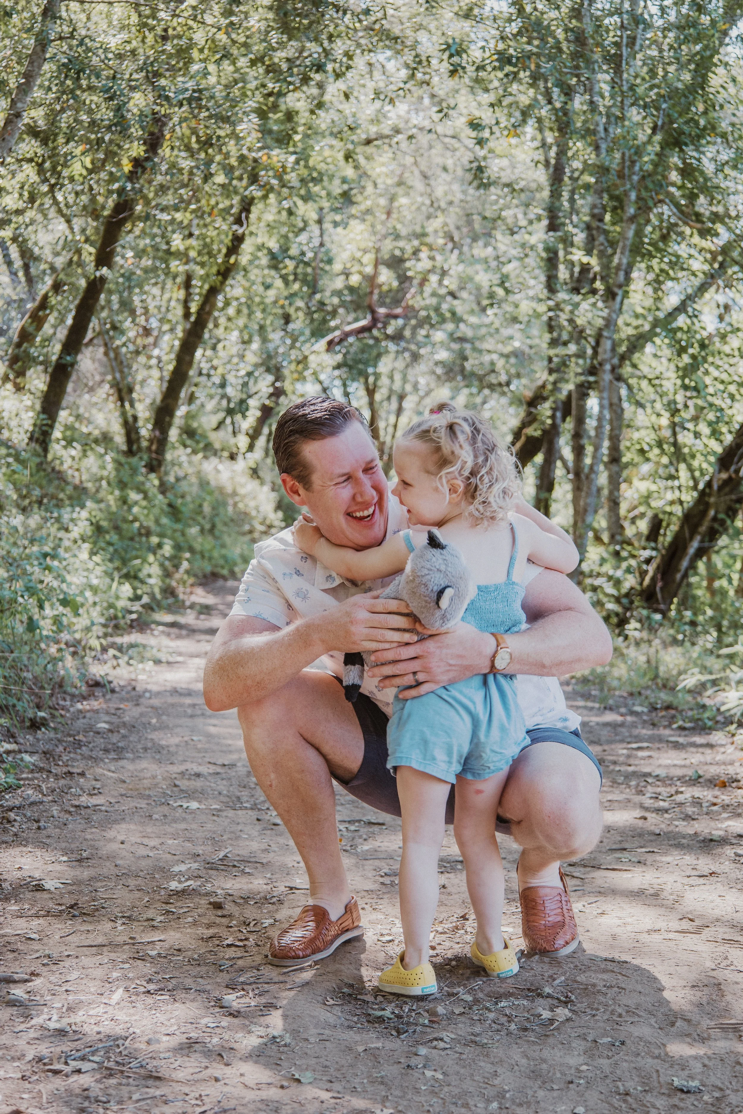 Dad crouching with his toddler on a wooded trail during a family session