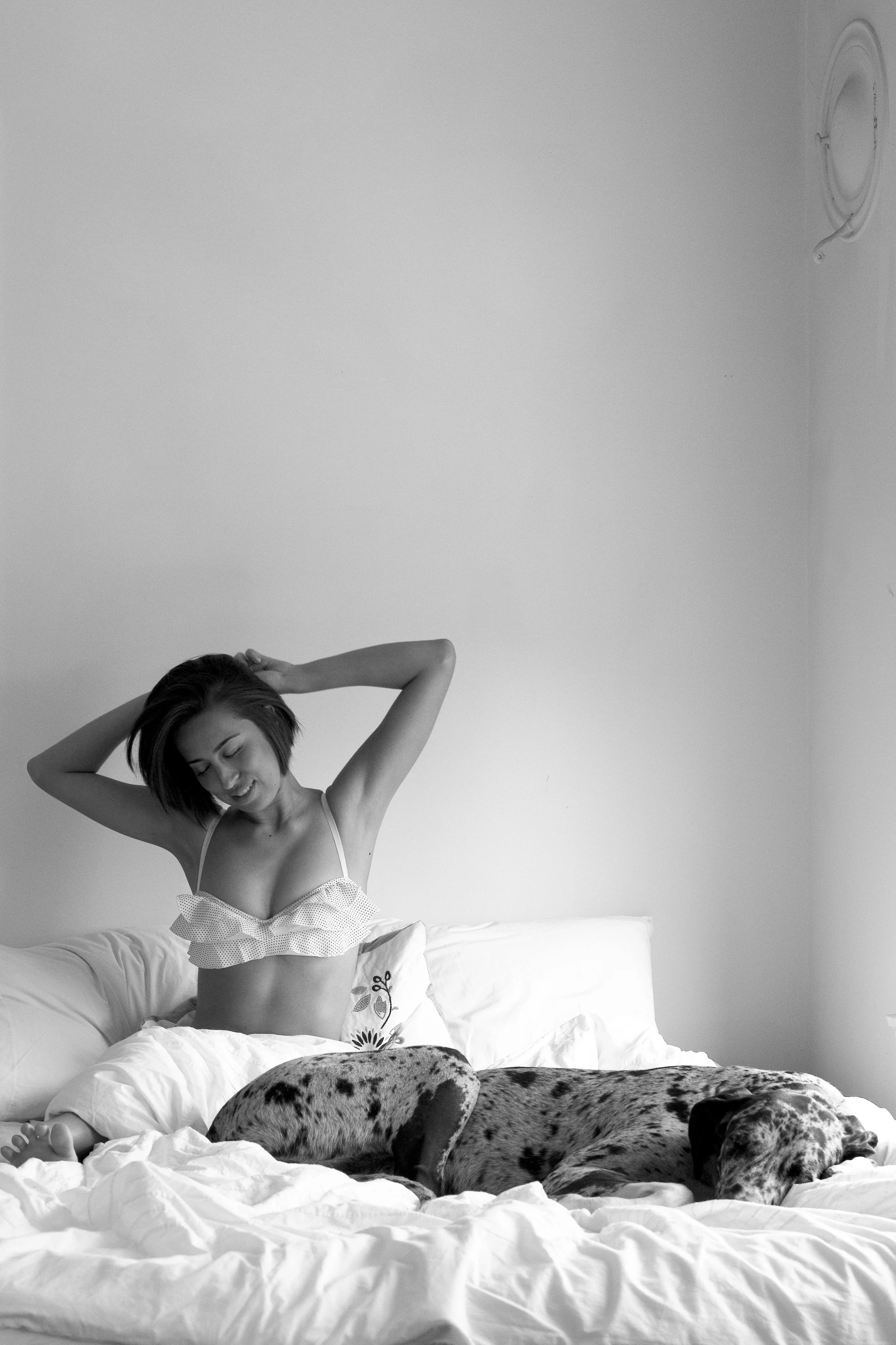 Black and white portrait of a woman stretching in bed beside her Great Dane