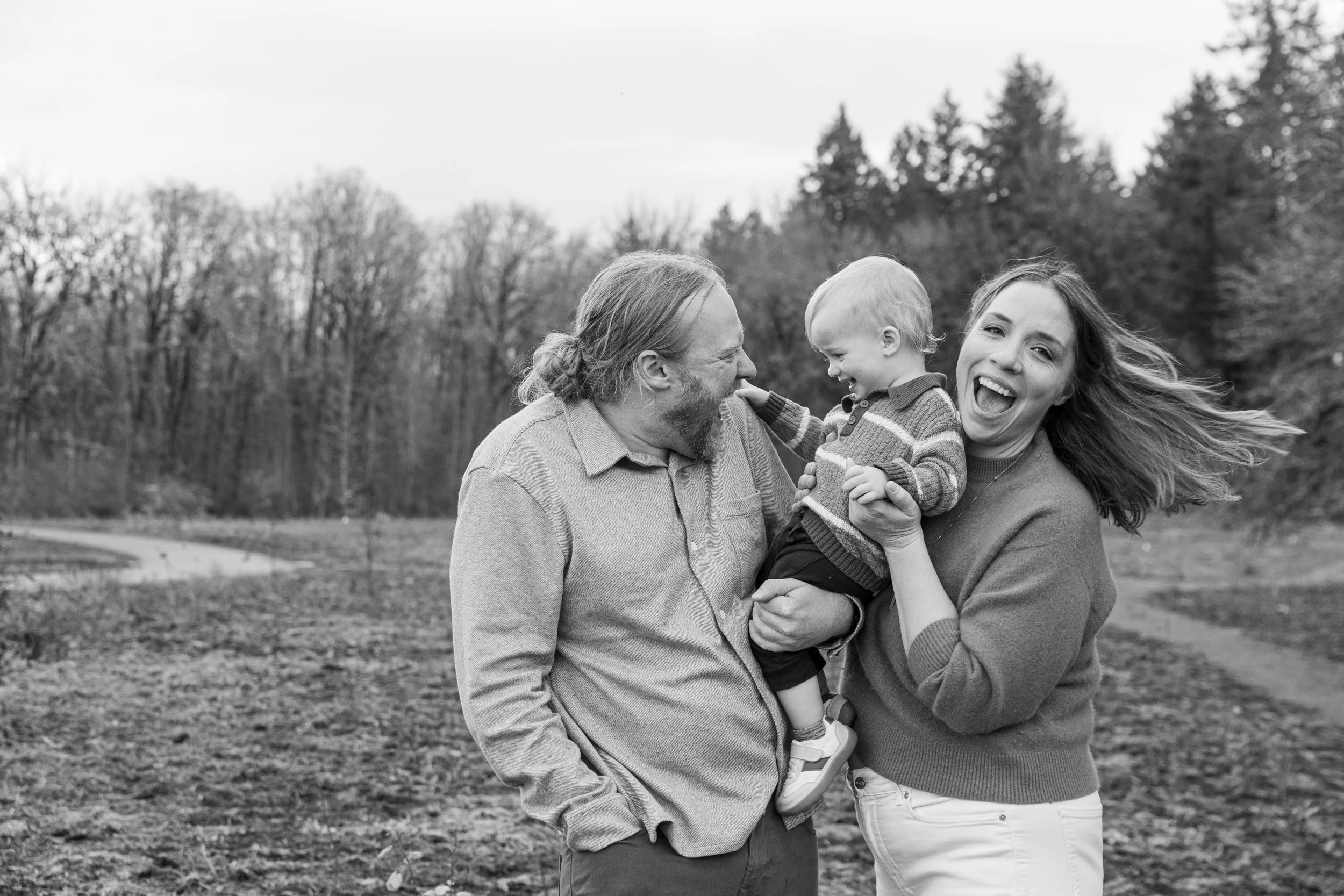 Family of three laughing together outdoors in an open field