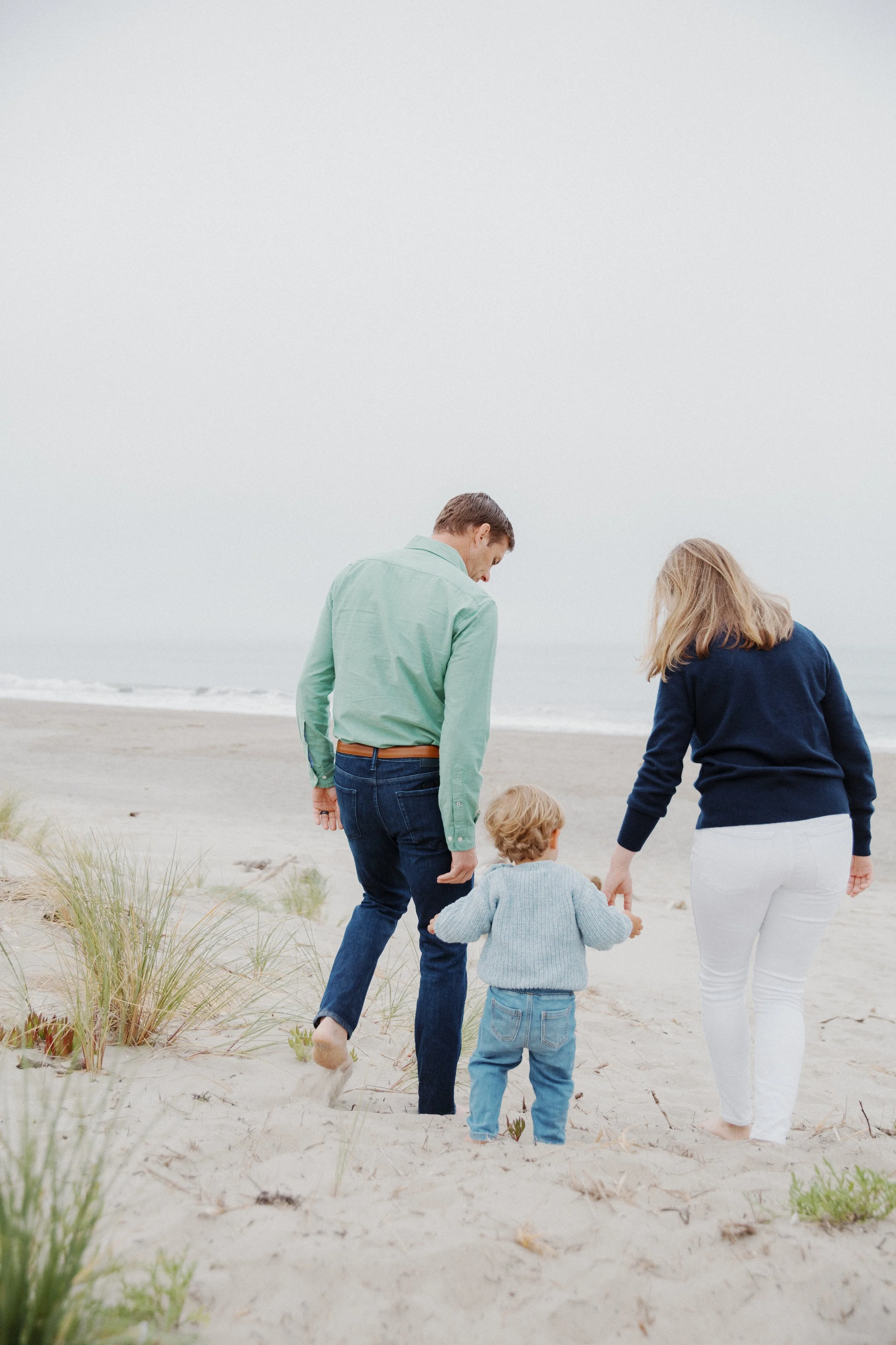 Family walking together along a grassy beach with their toddler