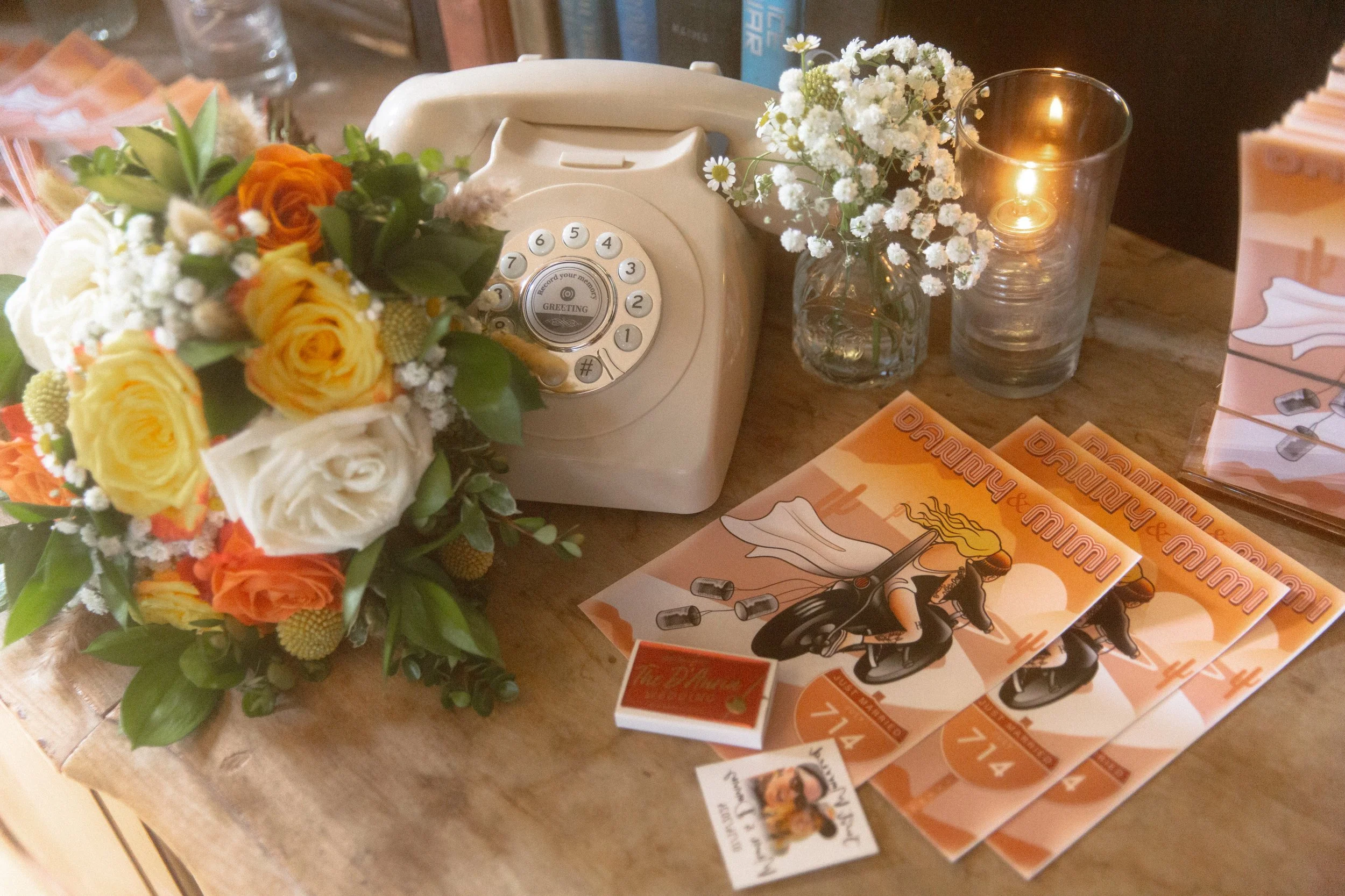 Guest book table with a vintage rotary phone, a bouquet and orange programs