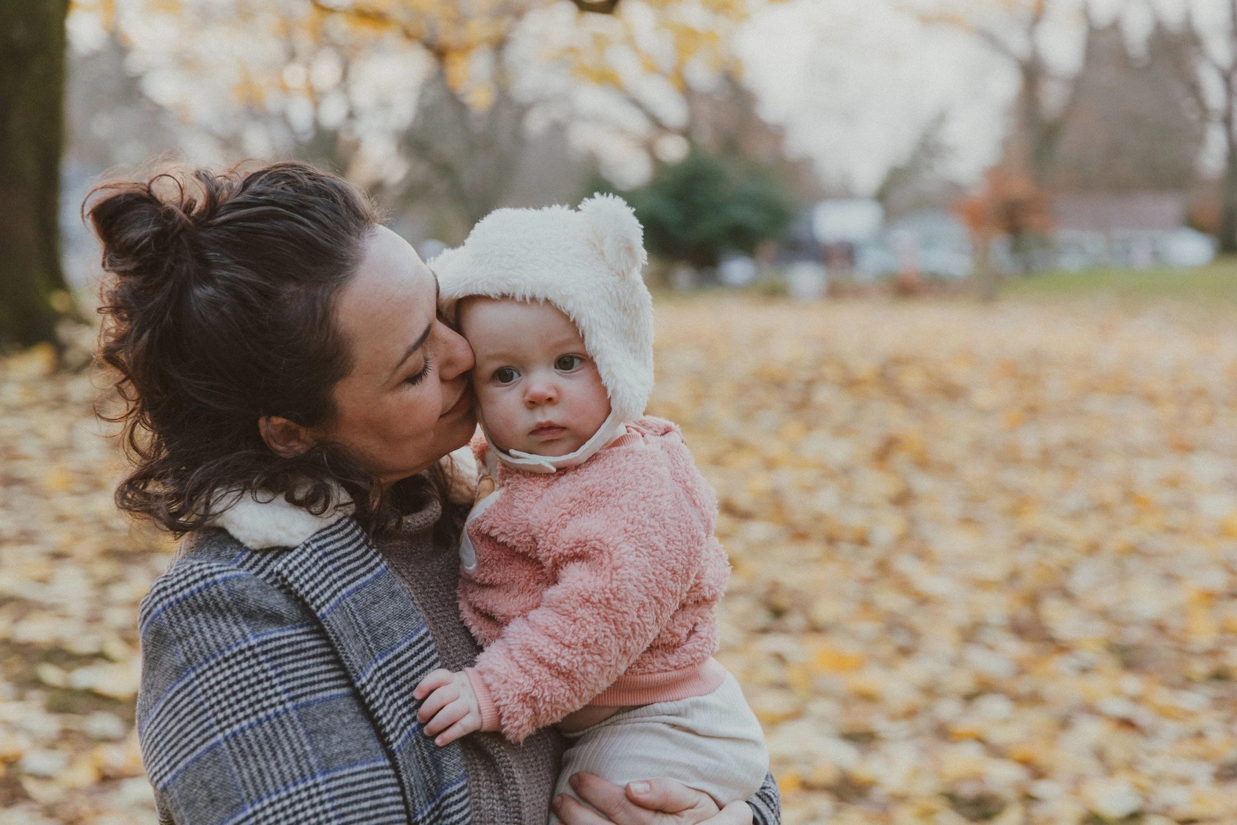 Mom kissing her baby in a bear hat among golden fall leaves