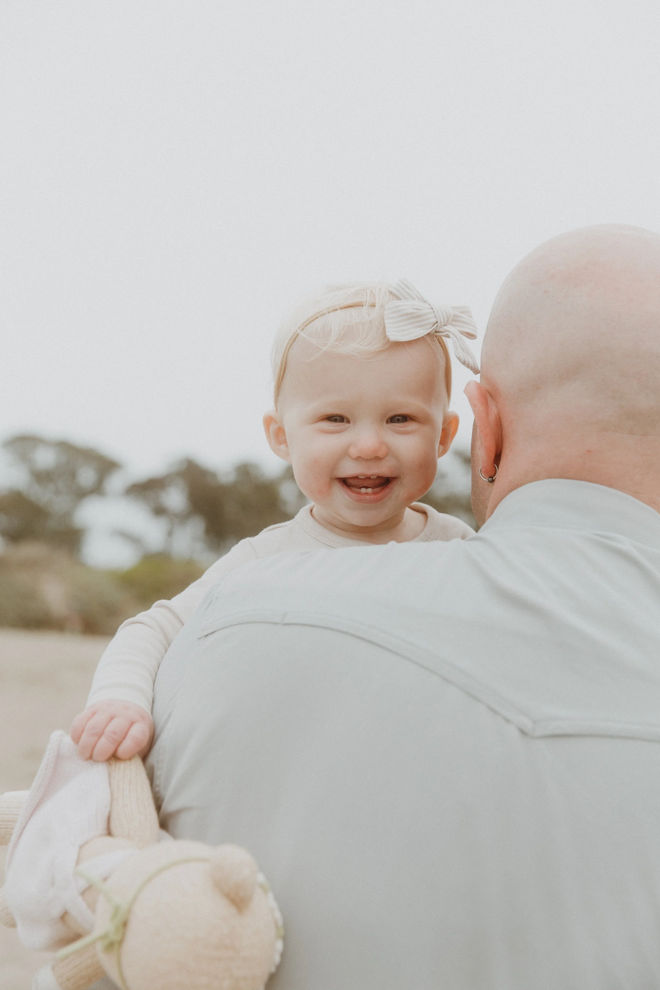 Laughing toddler looking over her dad's shoulder during a family session