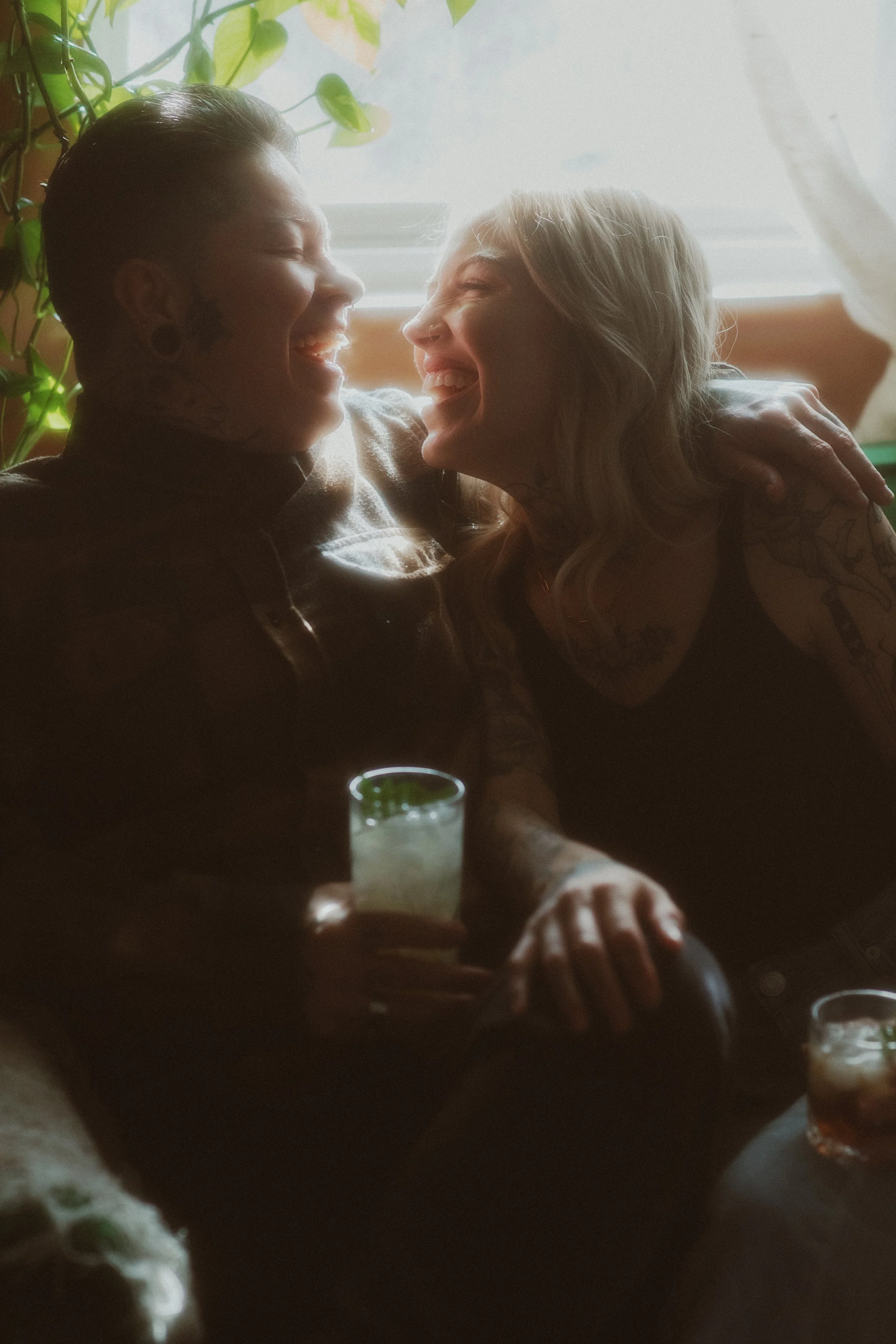 Couple laughing over drinks in a cozy, plant-filled room on their elopement day