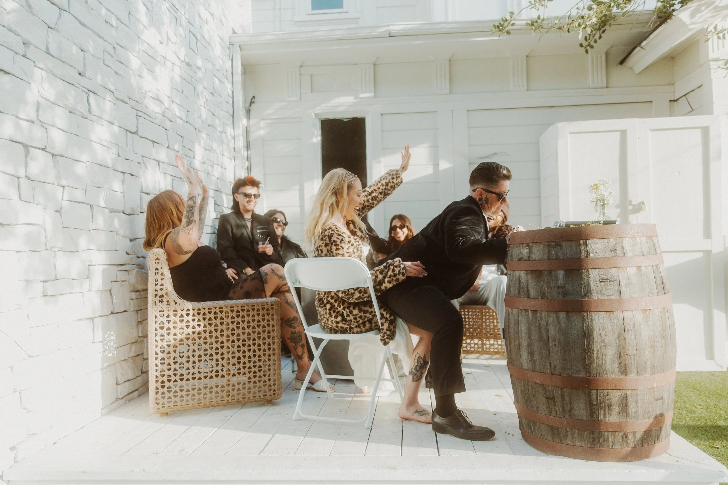 Wedding guests relaxing on wicker chairs beside a white brick building