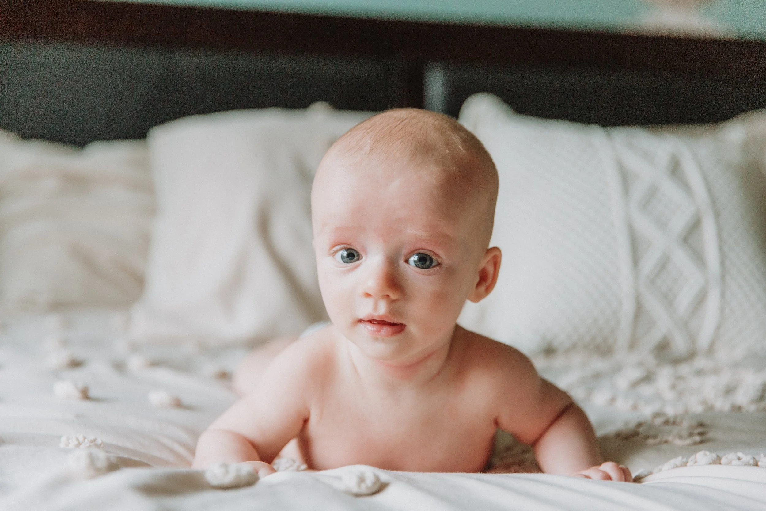Smiling baby propped up on a bed during a cozy at-home family session
