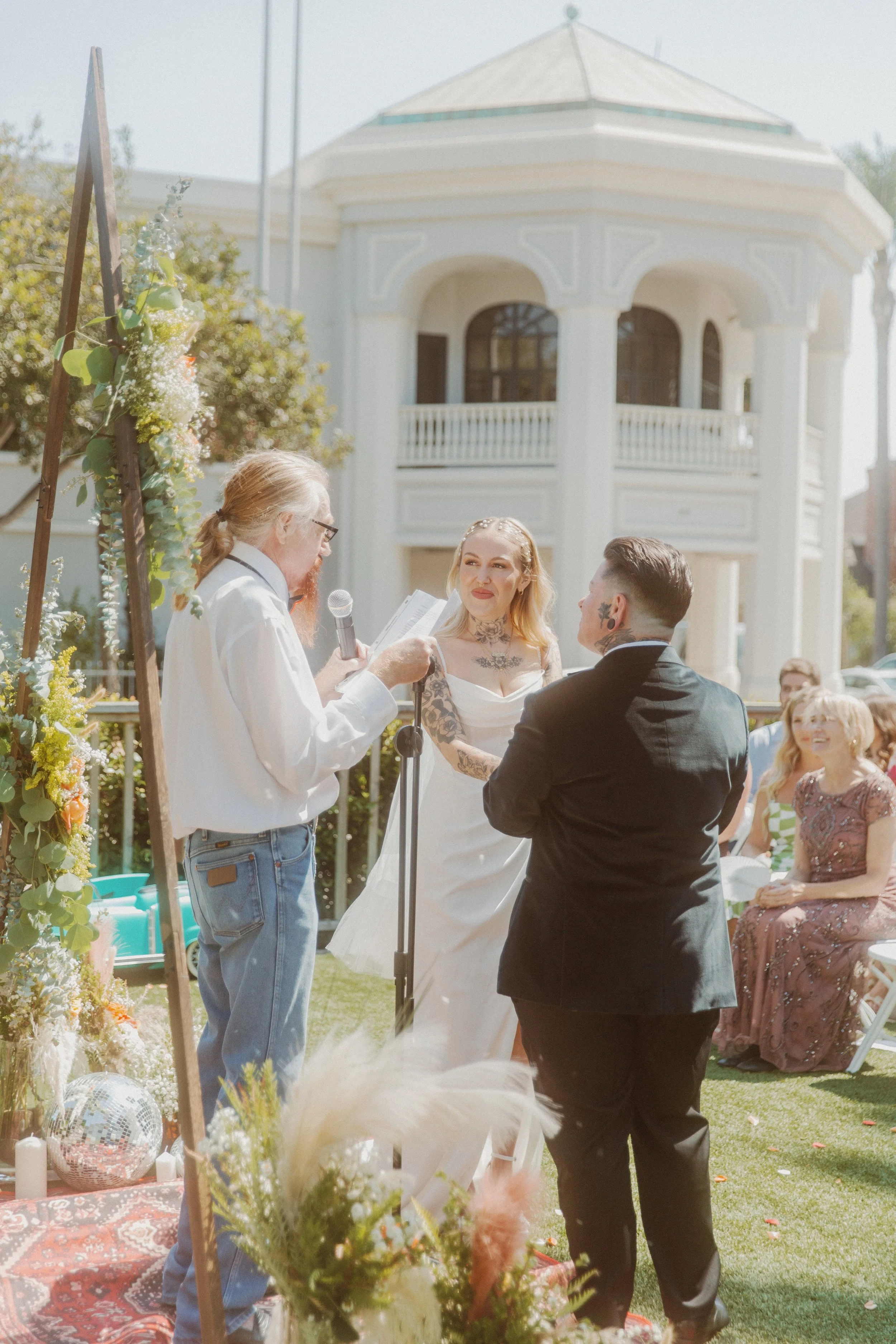 Couple and officiant during an outdoor ceremony in front of a white Victorian building