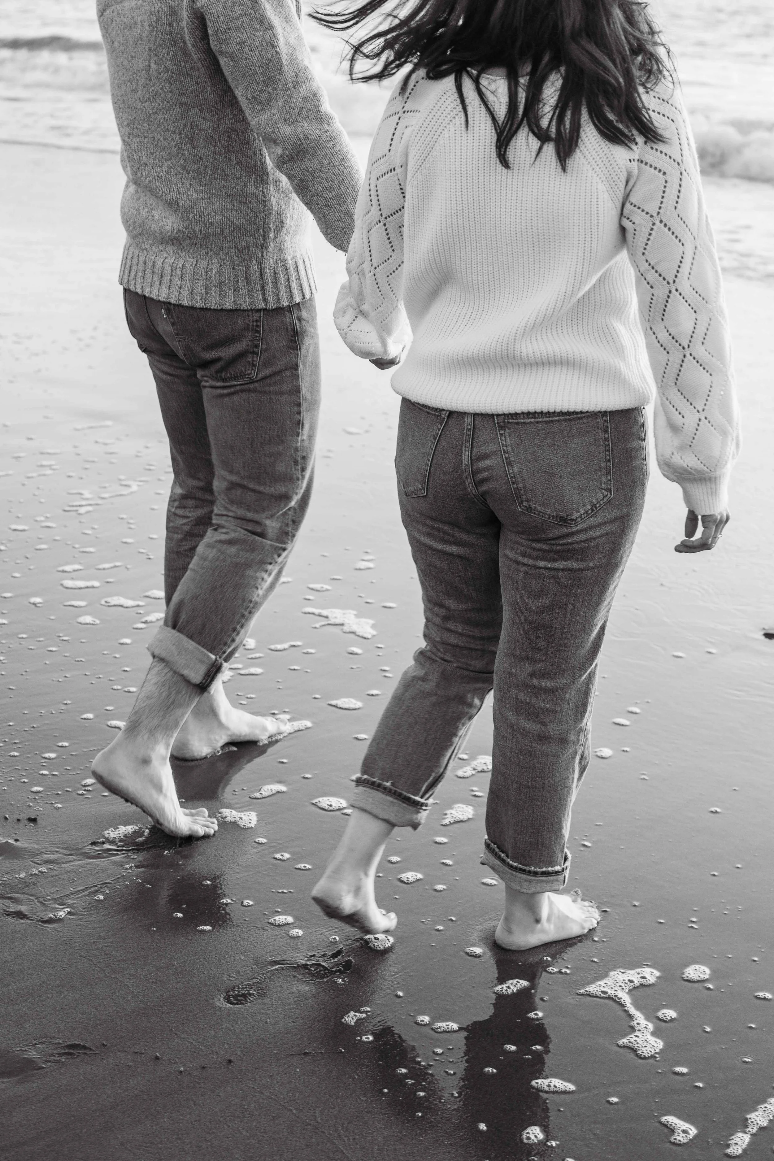 Couple walking barefoot along the shoreline holding hands